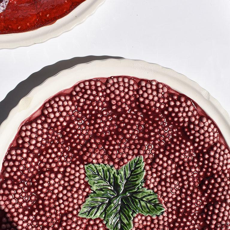 Set of seven ceramic Majolica fruit plates. This beautiful set features two maroon raspberry plates, two apple plates, two strawberry plates and one lemon plate. Edges are thumbprint or scalloped. Each plate is covered in its respective fruit, with