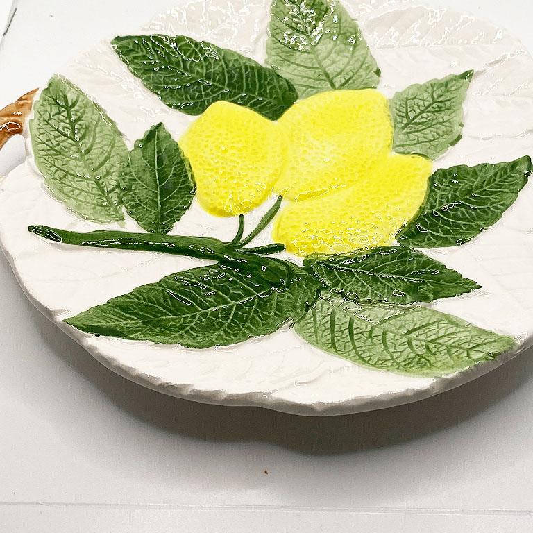 A small round majolica ceramic lemon plate. This plate will be great displayed on a wall or used at your next party to display food. Bright yellow lemons and green foliage decorate the top of this dish, with brown glazed handles on the side.