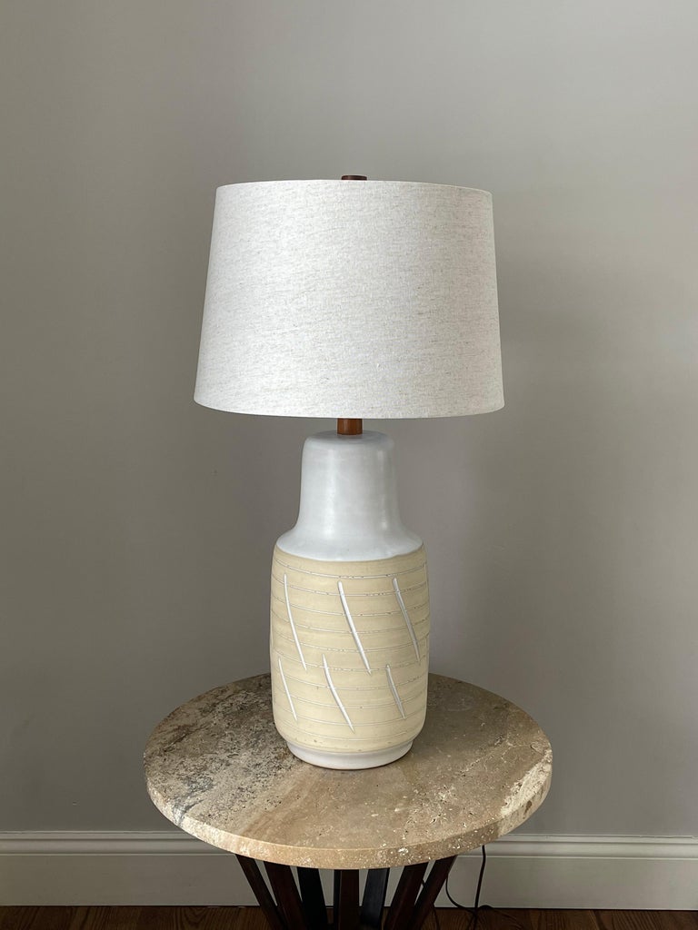 Classic ceramic table lamp by ceramicist duo Jane and Gordon Martz for Marshall Studios. Features a large ceramic body with flat white ceramic portion and matte tan body. Simple incised detail accompanies the colors well. Walnut neck and finial. New