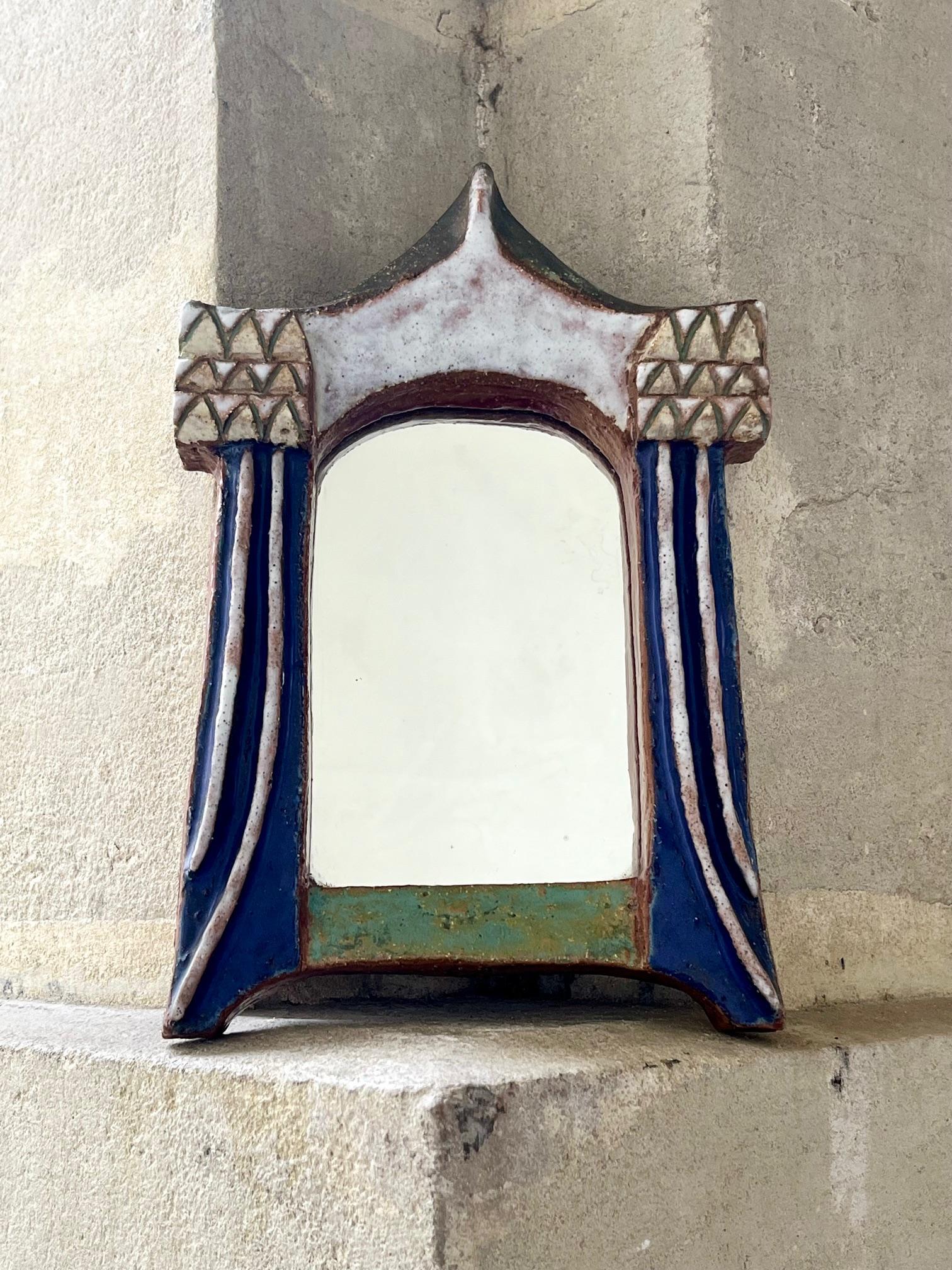  Miroir des Argonautes. 
Cadre en forme de tente, céramique émaillée dans les tons blanc, bleu, ocre et vert. 

Signé au dos 