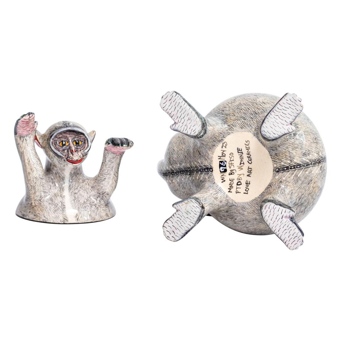 This ceramic monkey box is a unique and whimsical creation handcrafted in South Africa. Its clever design features a removable lid that forms half of the monkey's body, with the other half serving as the base. Rendered in shades of grey and black,