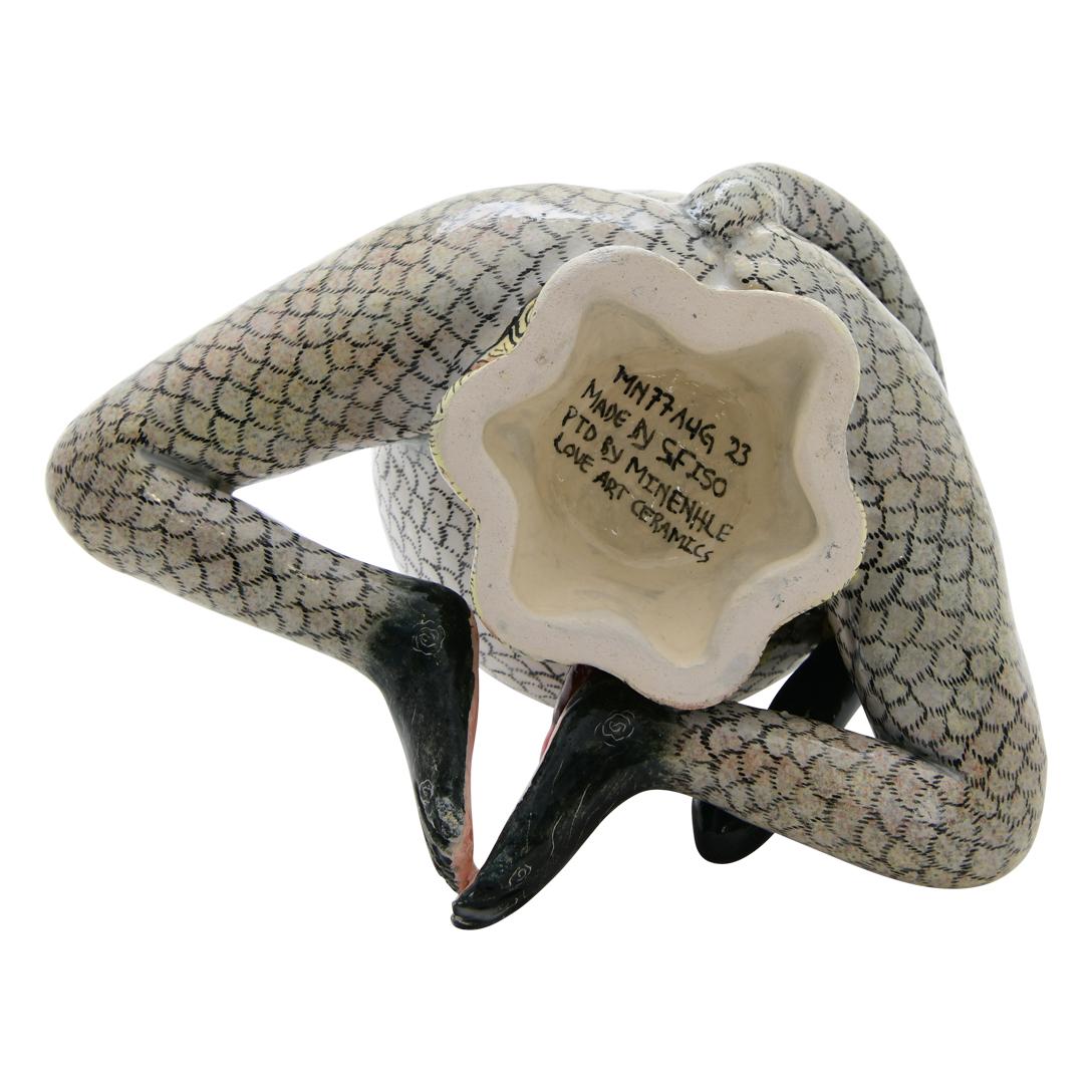 This handcrafted ceramic monkey box is a delightful creation from the talented artisans of South Africa. Shaped like a seated monkey enjoying a banana, its clever design features the monkey's body as the lid, adding a playful touch to the piece.