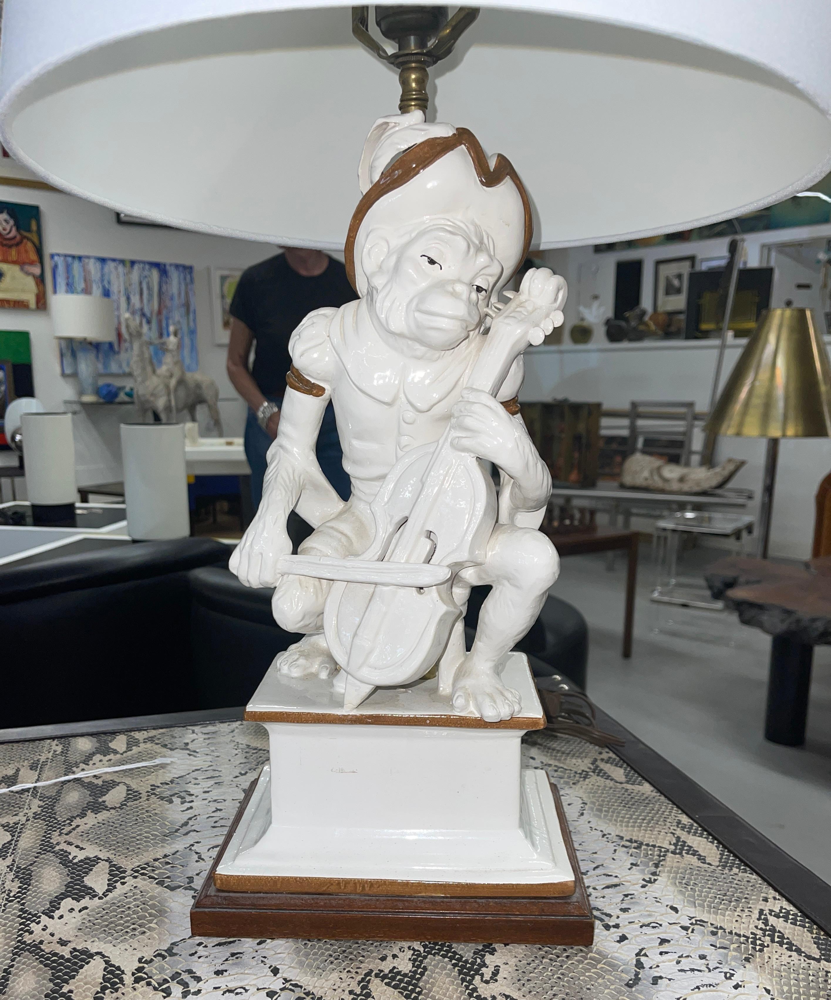 Whimsical Ceramic or Majolica Italian Monkey lamp. The monkey is playing a musical instrument, likely a violin. Mounted on a wood base. The lamp is functioning and likely dates to the 60's or 70's. There is a noticeable chip to the base, pictured