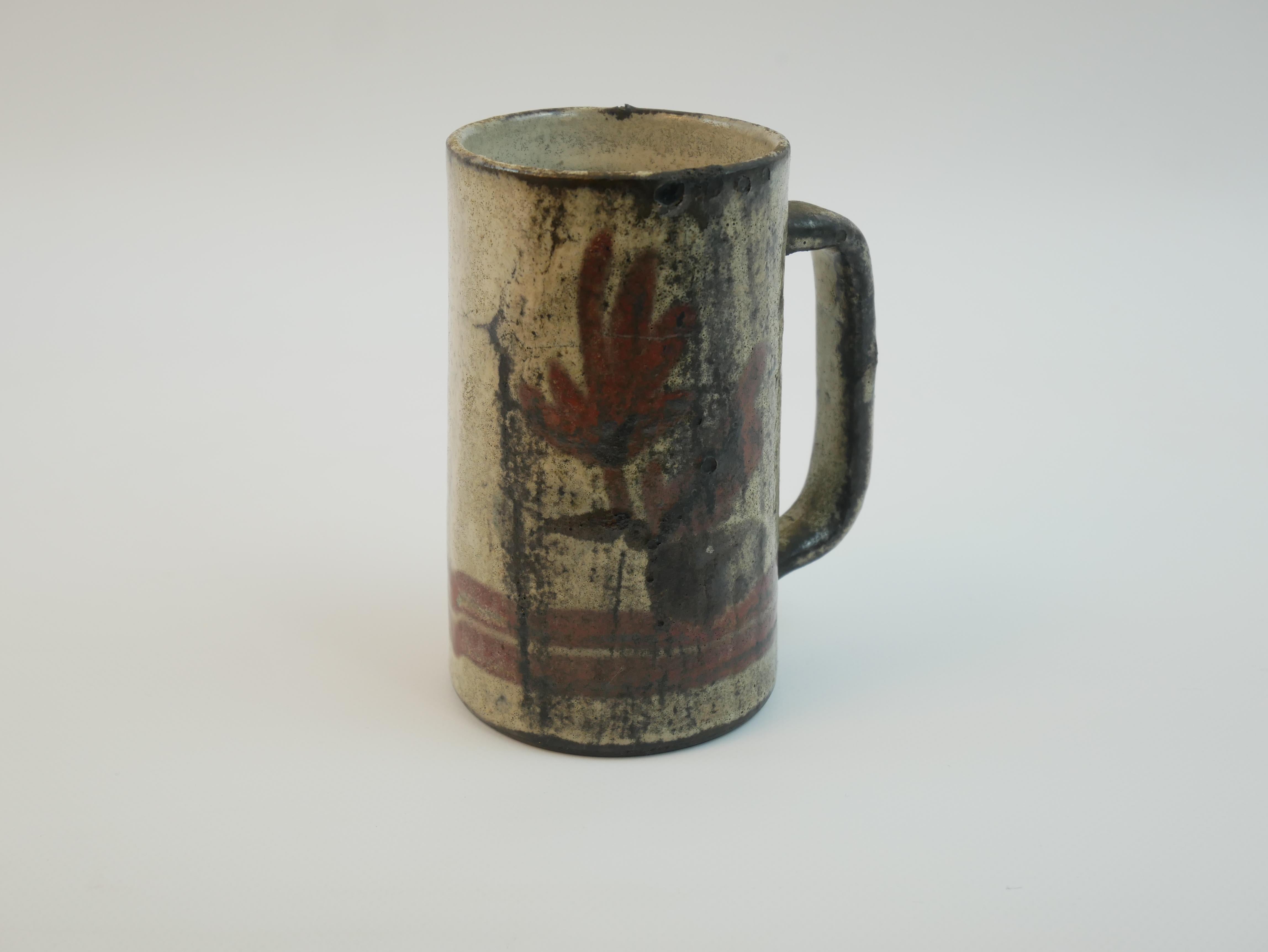 Es handelt sich um eine Vintage-Keramik-Tasse, die von Gustave Reynaud in Vallauris in den 1950er Jahren hergestellt wurde. Die für ihren rustikalen und zugleich künstlerischen Charme bekannte Tasse ist mit einer matten Glasur in Erdtönen versehen