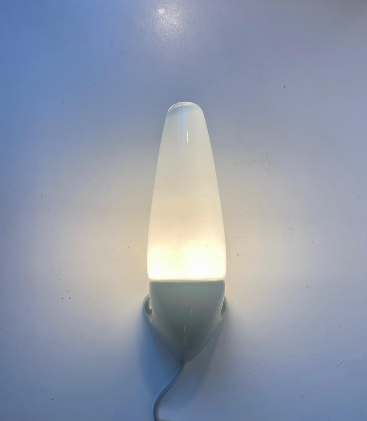 Wall sconce suitable as bathroom or outdoor lighting. Designed by Prince Sigvard Bernadotte for the swedish company Ifö during the 1960s. Cucumber glazed ceramic mount with a white opaline glass shade. 2 way mount - either shade facing downward or
