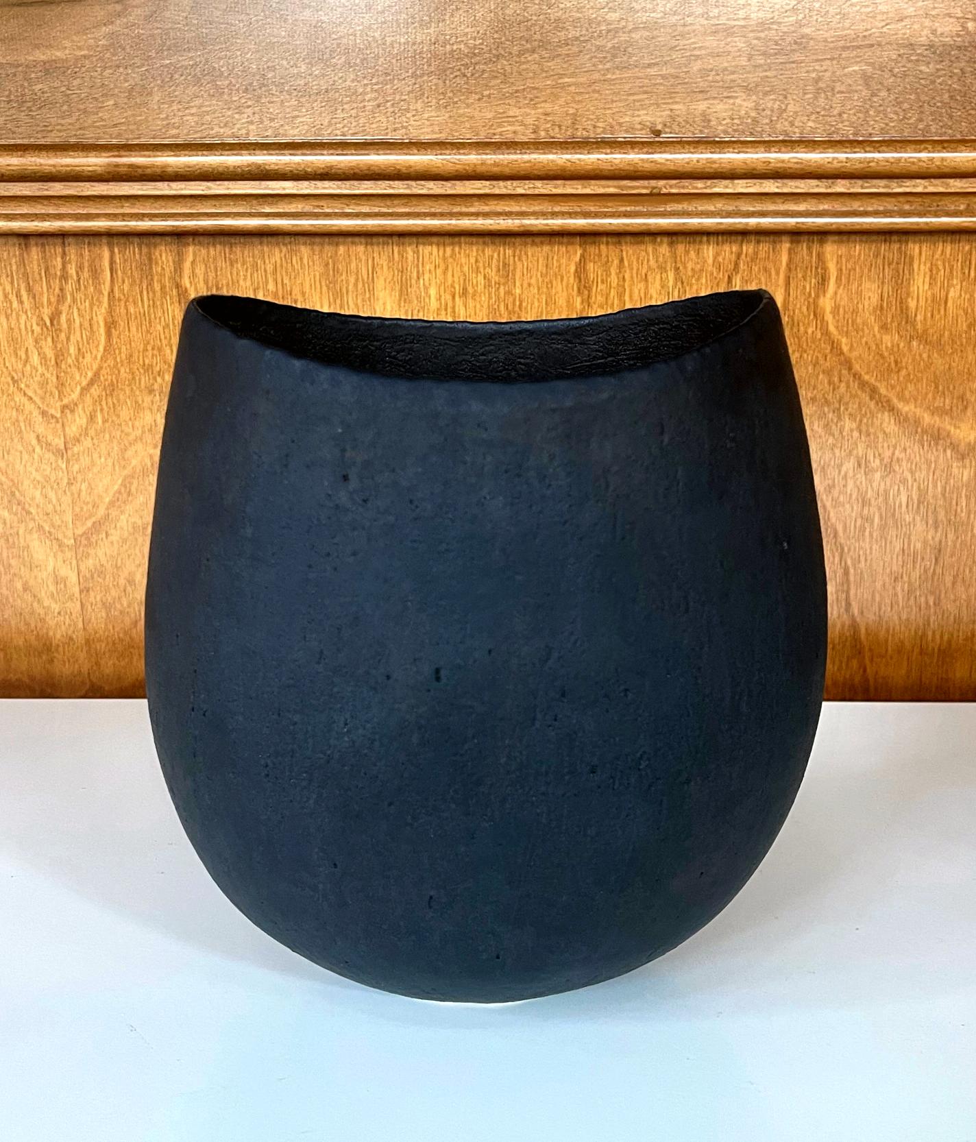 Un récipient en grès de forme ovale à bord trempé et émaillé par le céramiste de studio britannique John Ward (1938-2023) vers 1997. La forme de ce récipient est minimaliste et volontairement ambiguë, entre pot et vase. Être organique et terreux
