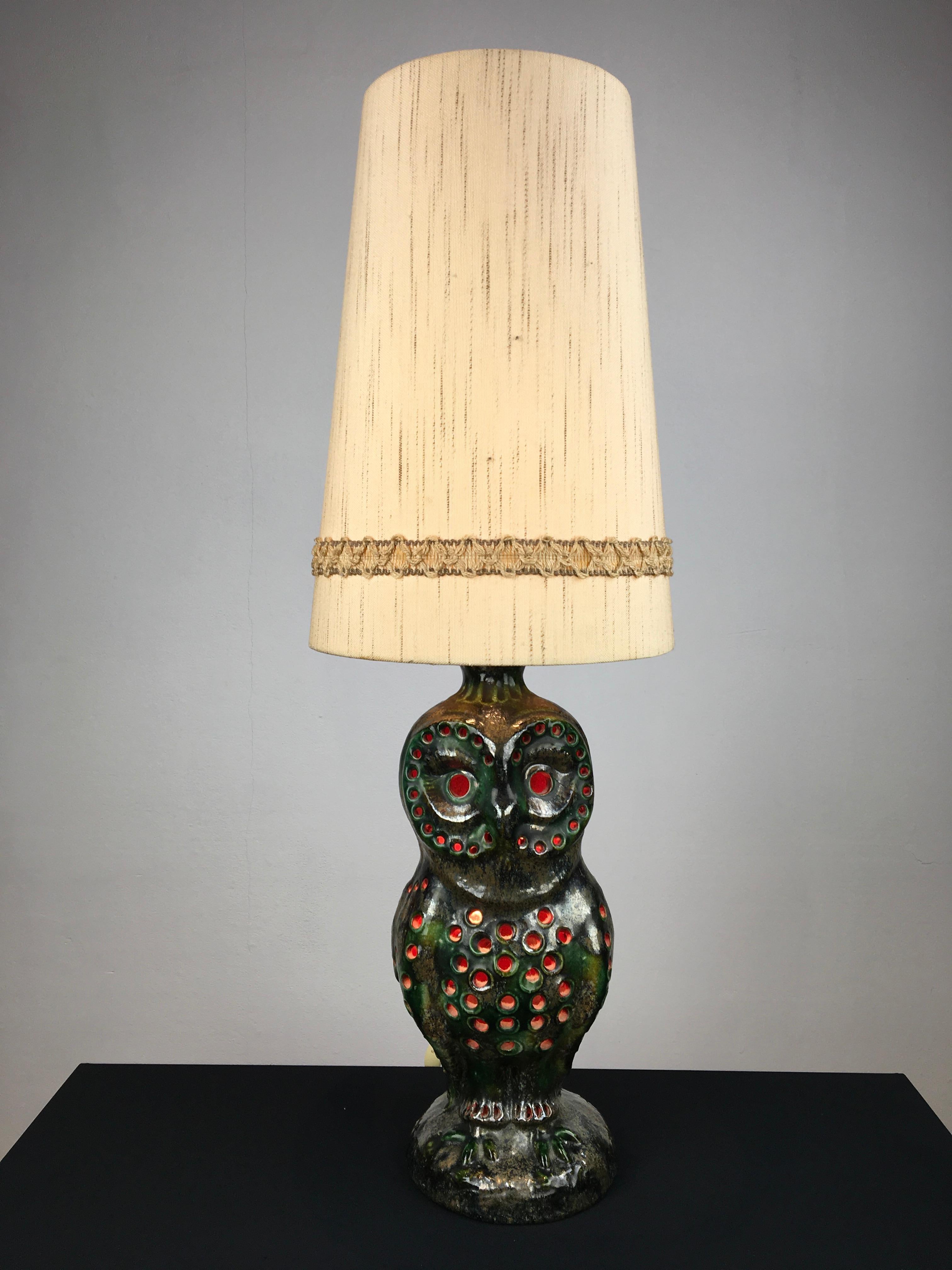 1970s ceramic owl table lamp.
This large vintage ceramic table lamp is in the shape of an owl and was made in Germany. This bird light has the colors green, brown, orange and a gold, bronze with silver touch. It has 2 fittings for E27 bulbs: 1 on
