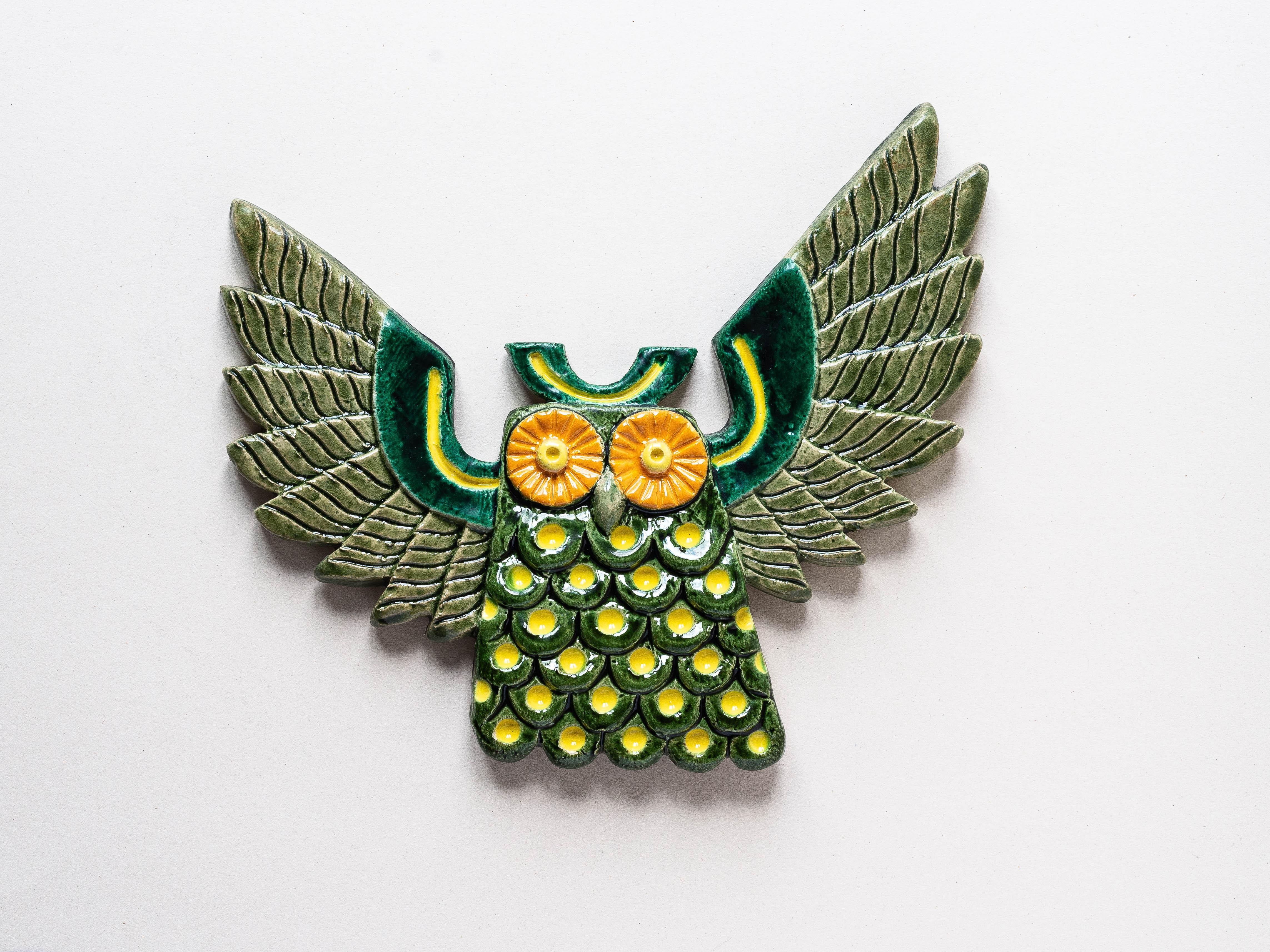 This ceramic owl wall sculpture dates from the 1970s. 

It comes from the “Kergibot” pottery workshops, located in Brittany, France. 

The ceramic is glazed in green, yellow, and orange. It features a very beautiful work in terms of color scheme and