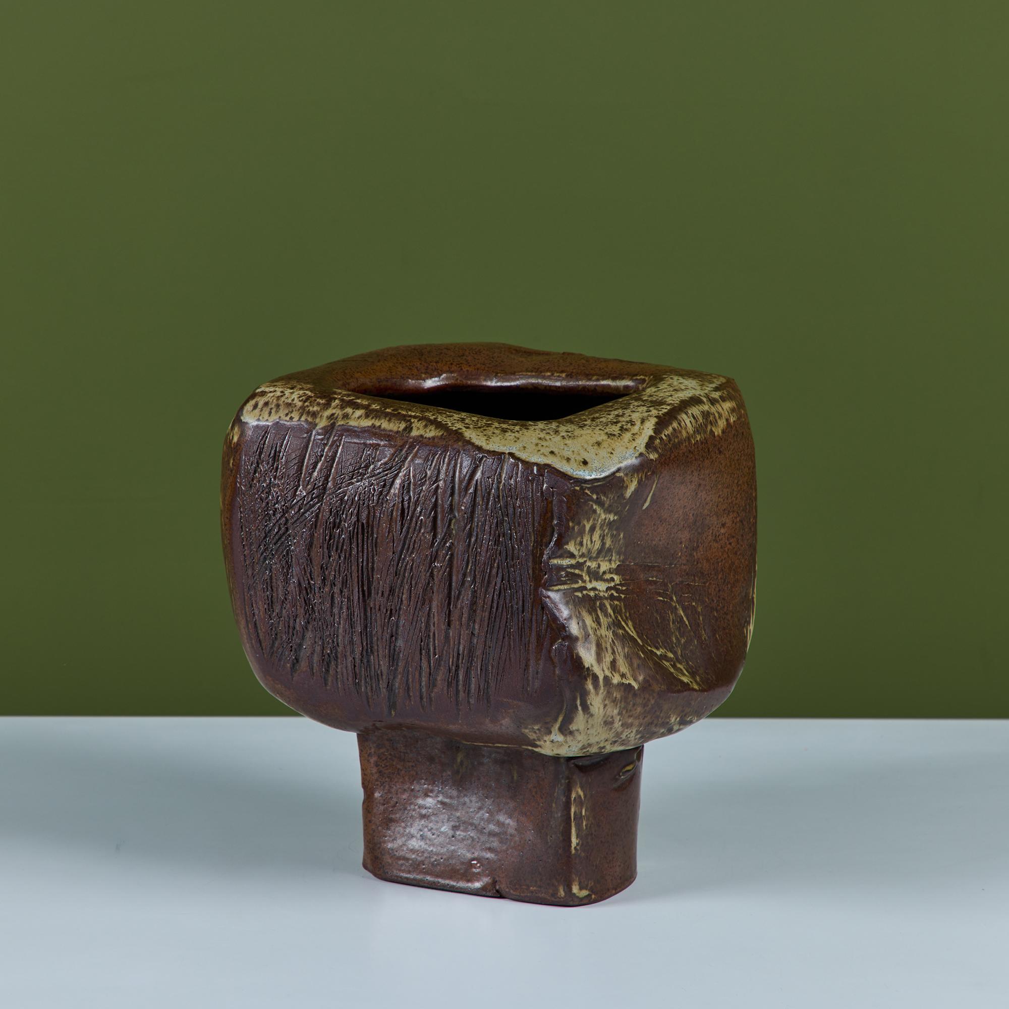 Vaso Ikebana a piedistallo smaltato di marrone. Il vaso presenta una forma cubica con spille floreali interne alla base del vaso. Il vaso poggia su un piedistallo con dettagli lineari incisi su due lati della forma.

Dimensioni
9,5