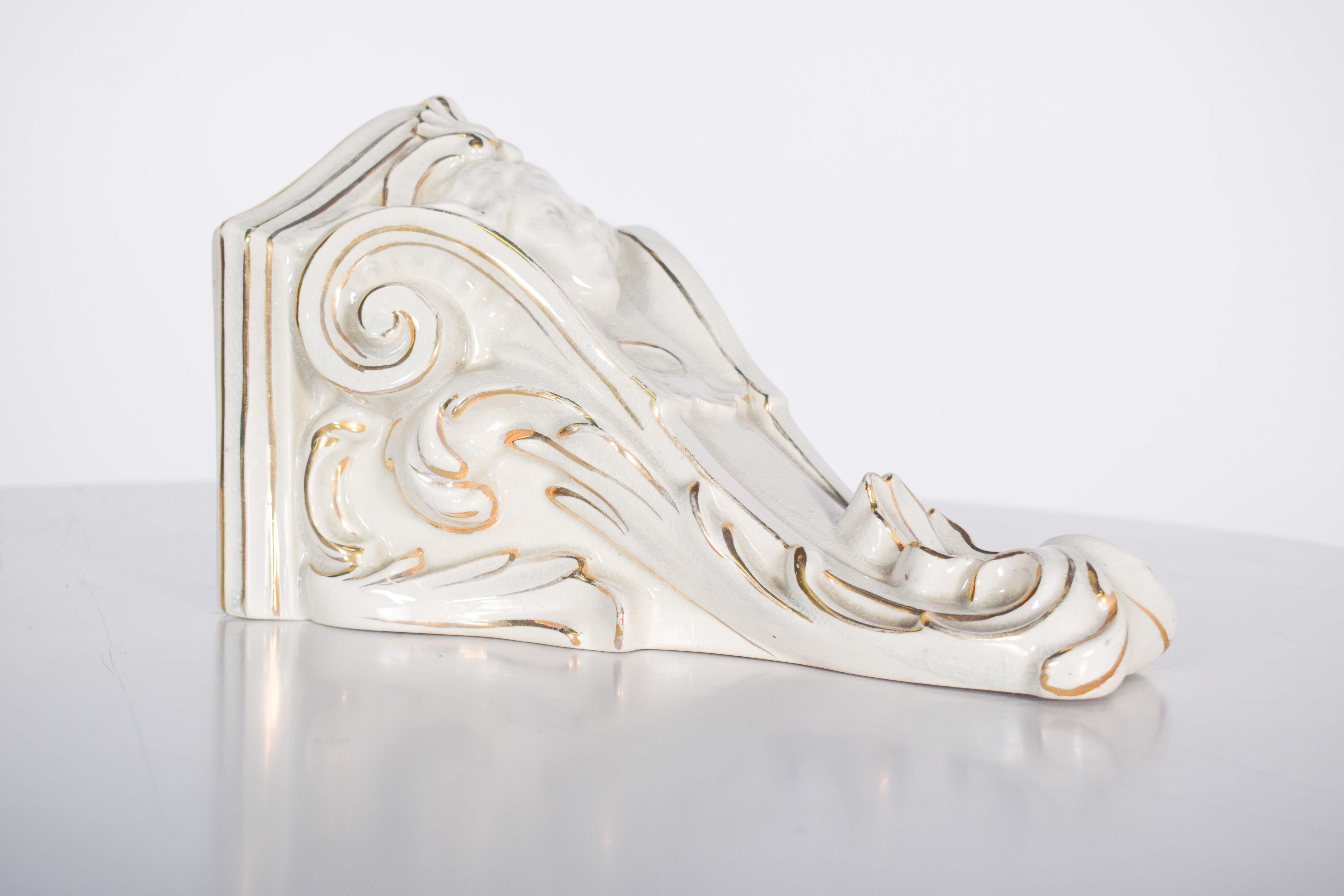 Piedistallo in ceramica. Decorata in oro e bianco, presenta un volto, foglie e volute in rilievo.
Le foglie e le volute in rilievo sono realizzate con precisione, creando un effetto tridimensionale che trasmette un senso di movimento e fluidità.