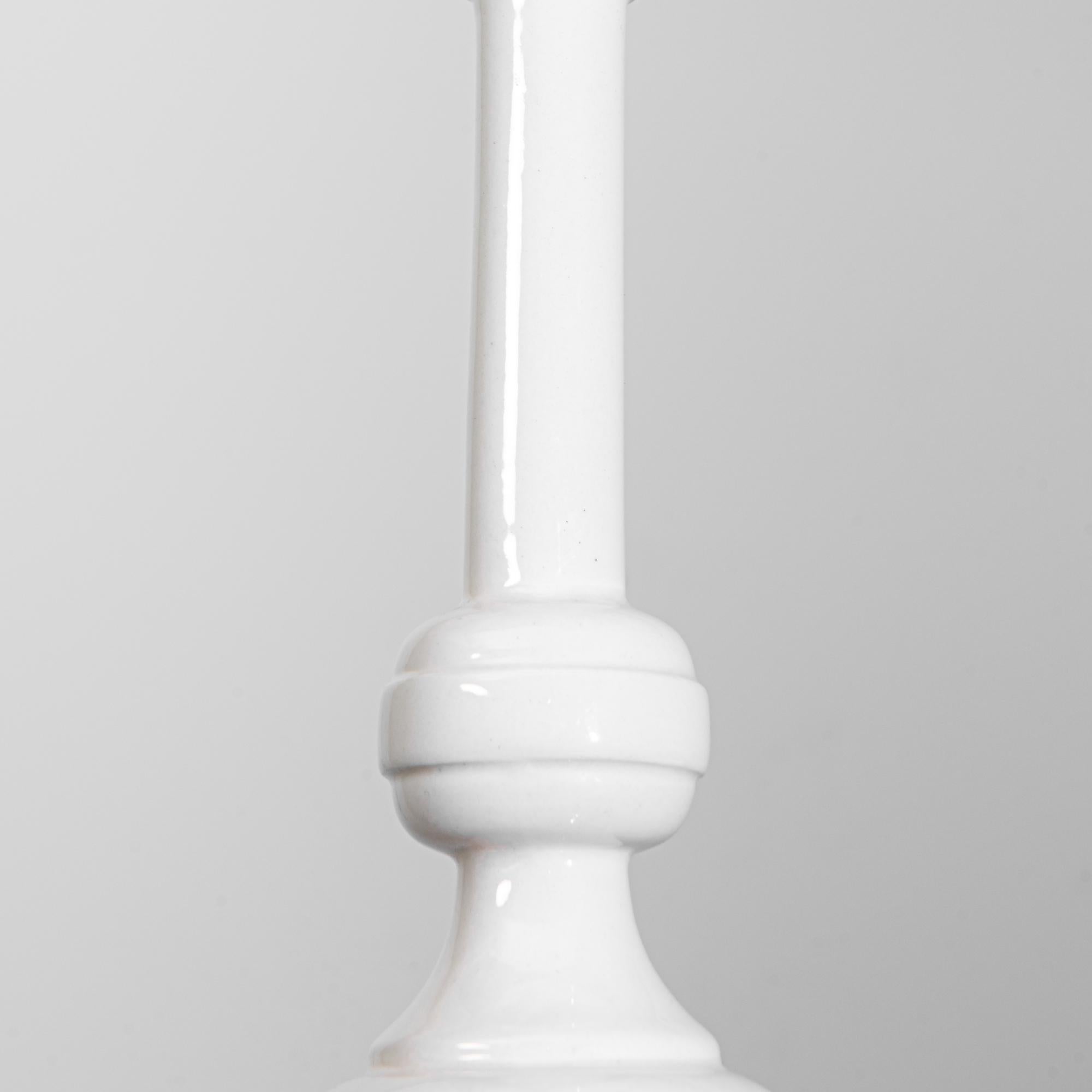 Con una seducente lucentezza, questa lampada a sospensione in ceramica vanta un'elegante forma tornita sottolineata dall'impeccabile smalto bianco. Forme simili a quelle di un tornio sospendono una lampadina elettrica, aggiungendo un elemento