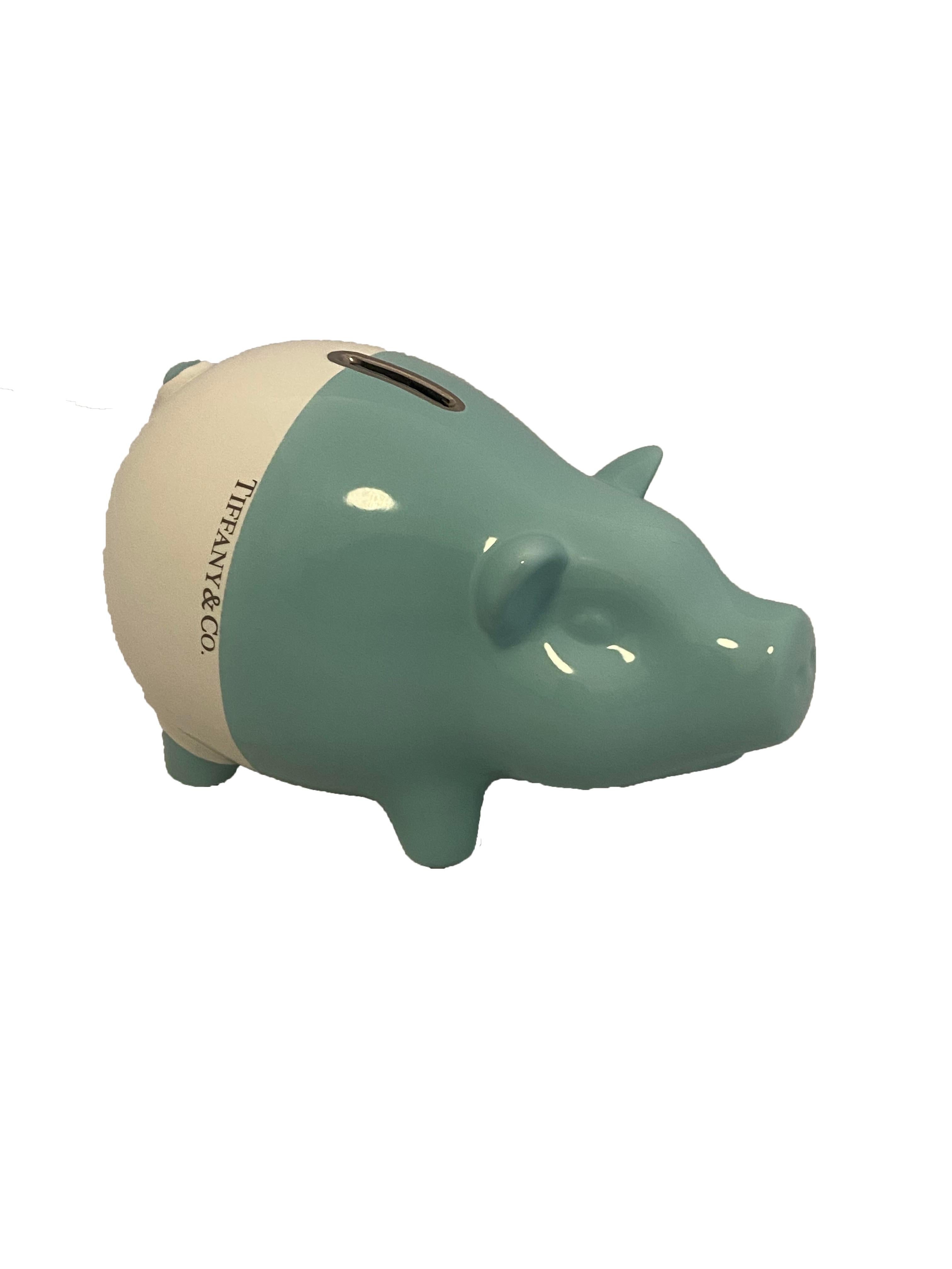 White and blue ceramic piggy bank from Tiffany & Co. Cute piglet shaped money bank crafted by Este Ceramiche in Italy and hand painted in the labels signature Tiffany blue and white with accent silver toned money slot at the top. Blue at the front