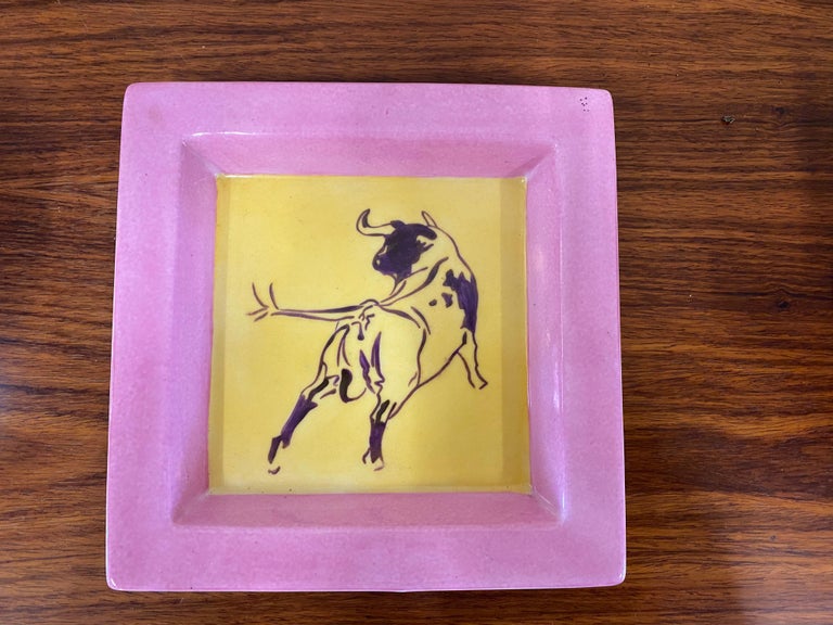 Colorful halltray with bull motif. The square ceramic comes from France and is from the 1960s. On the yellow glaze is depicted in purple a hand-painted bull. The rim of the tray is colored in pink, framing the motif nicely. The shallow tray with