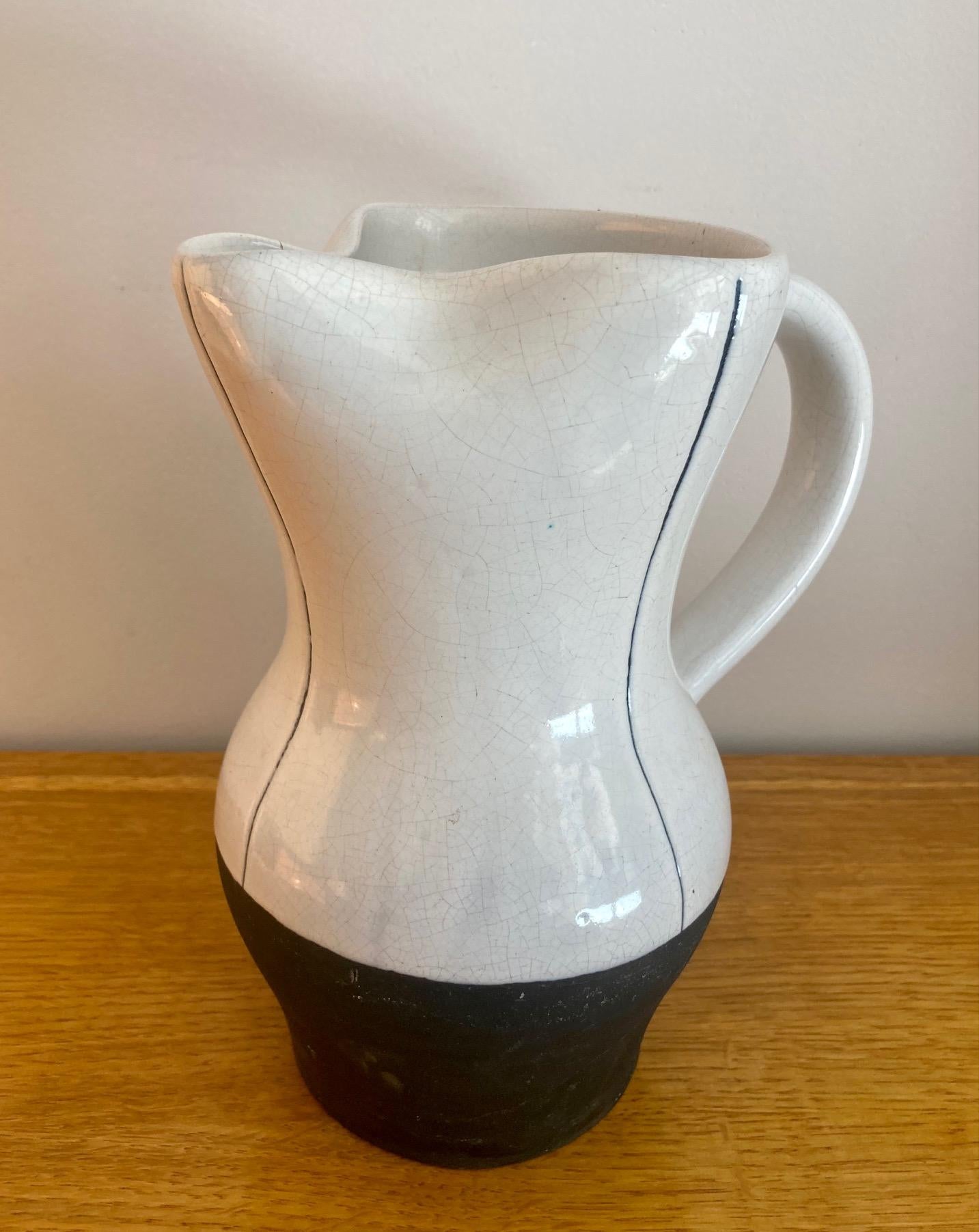 Two-tone ceramic pitcher in black slip and white glaze. 
Decorated with verticals stripes on the sides and on the handle. 
Vallauris, France 
Signed : 