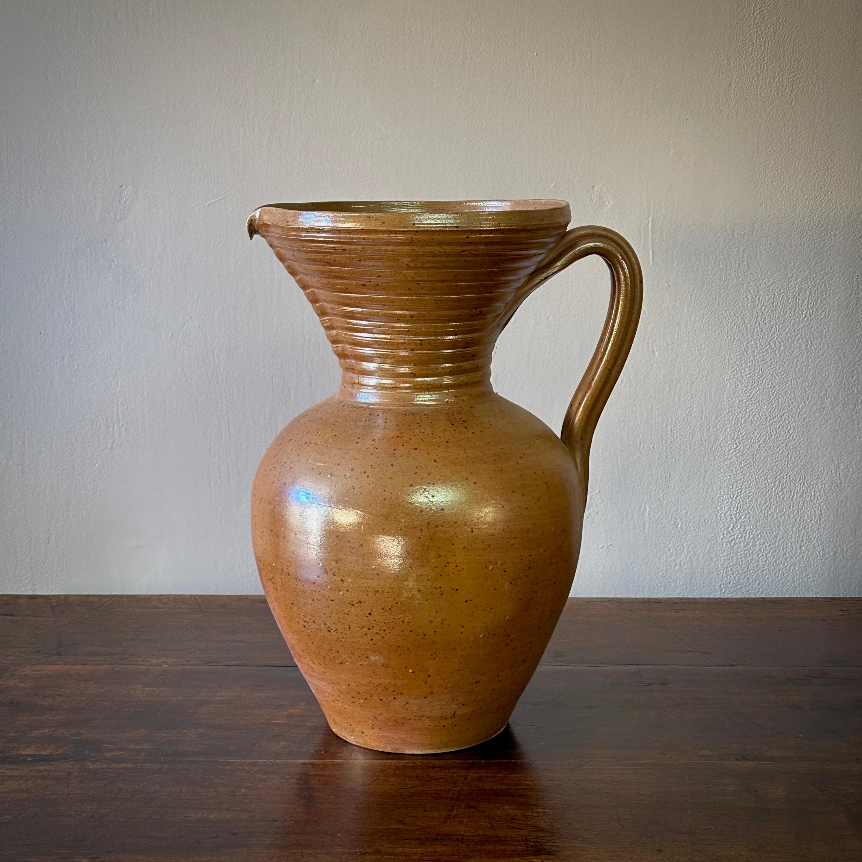 Questa brocca in ceramica francese esemplifica il design classico con il suo smalto color terra e la sua raffinata rusticità. La finitura lucente e la forma robusta ne fanno un oggetto funzionale e allo stesso tempo un gioiello decorativo, perfetto