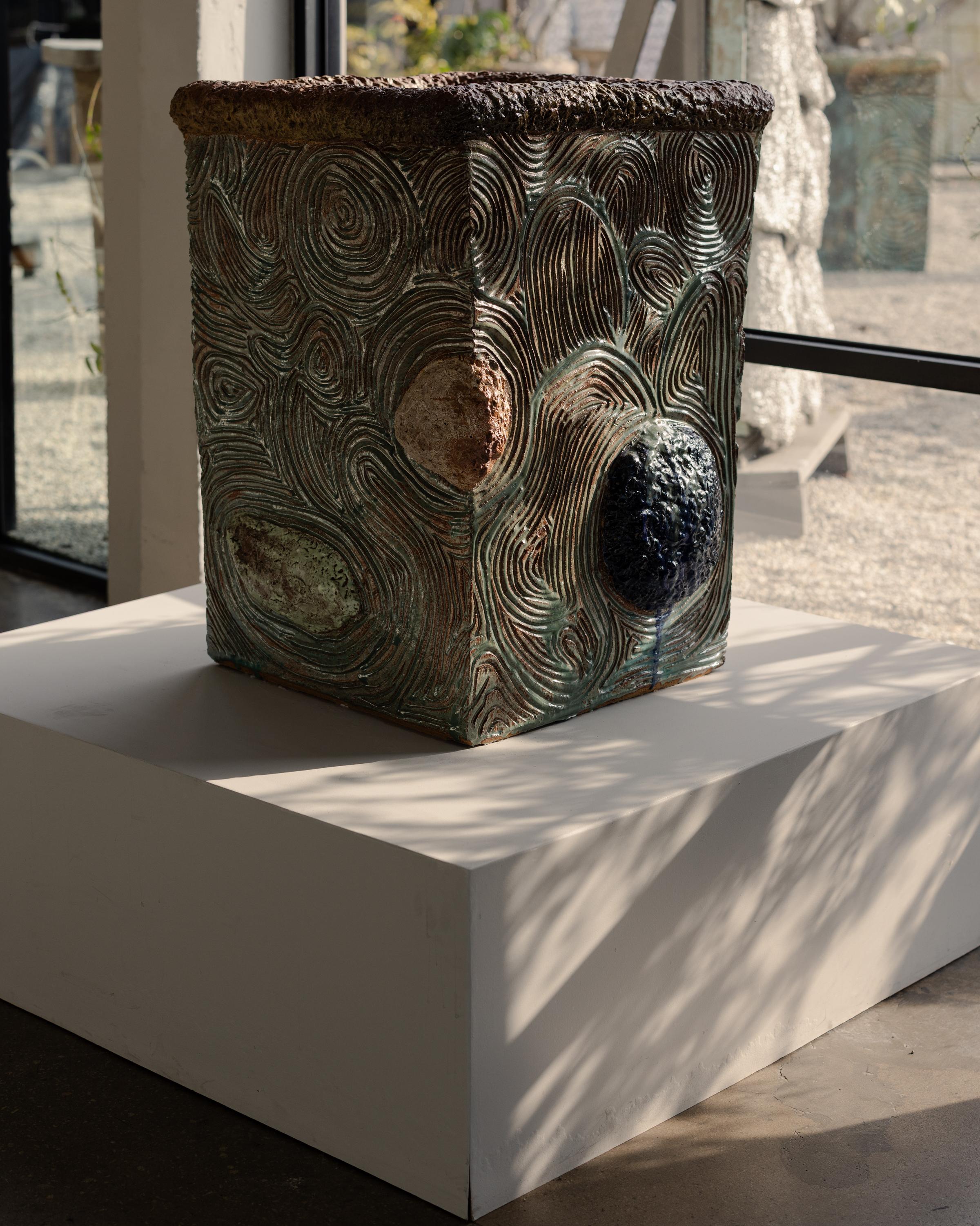 Una maceta de cerámica atrevida y táctil de la artista californiana Jody Baral. Esta pieza a gran escala presenta intrincados motivos arremolinados tallados a mano en sus cuatro lados, puntuados por esferas esmaltadas que sobresalen en ricos tonos