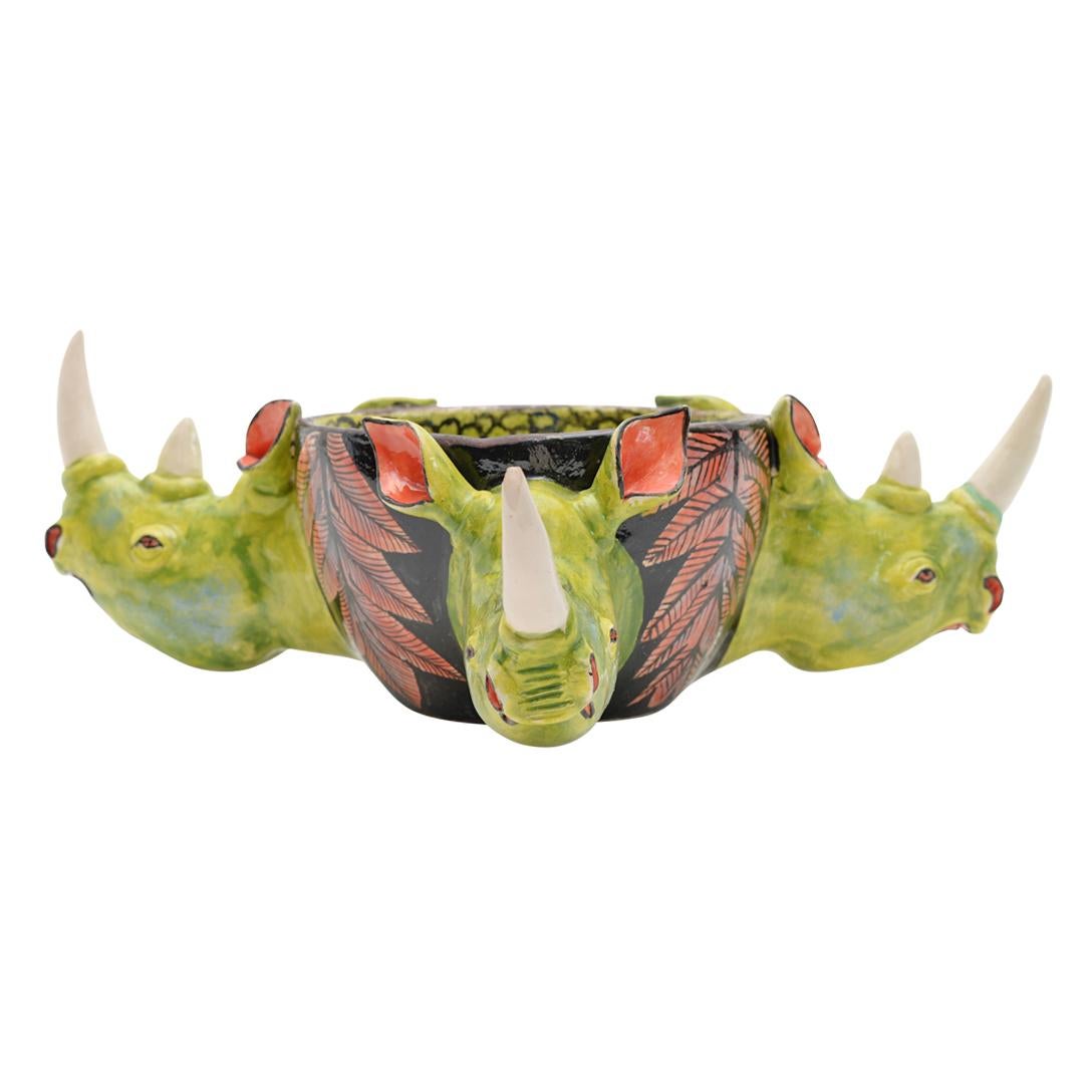 Imvelo Natural Art presents a unique ceramic Rhino peanut bowl from South Africa. Hand-sculpted by Teboho Ndlovu and hand-painted by Gabriel, this piece measures 4 inches high, 7 inches long, and 5 inches wide. The bowl features three rhino heads