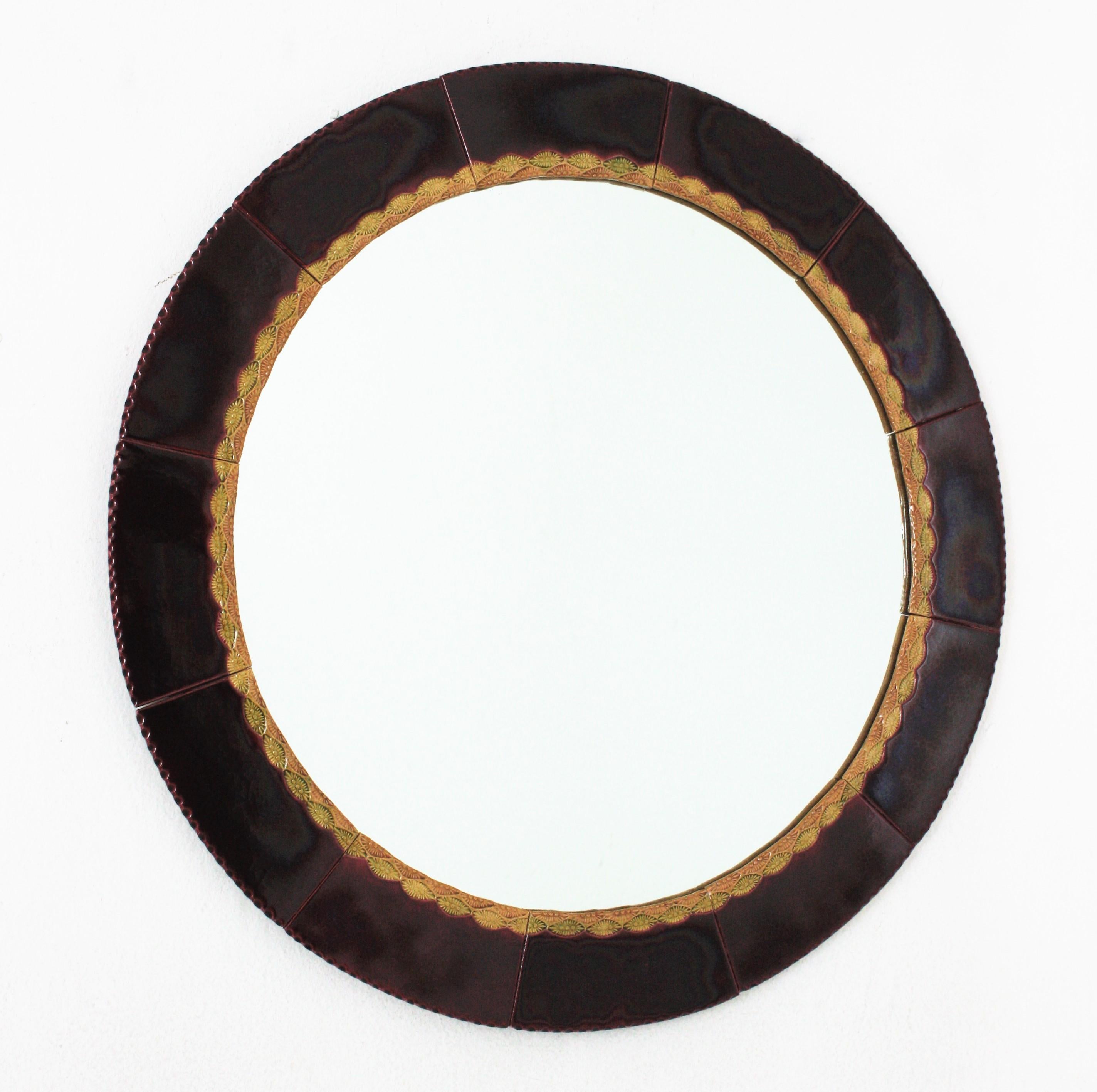 Eye-catching ceramic wall mirror. Maufactured in Spain, 1960s.
Circular Shape and large glass mirror surface.
The frame is made of glazed ceramic tiles in shades of burgundy / garnet. A decorative pattern in amber an yellow colors surrounds the