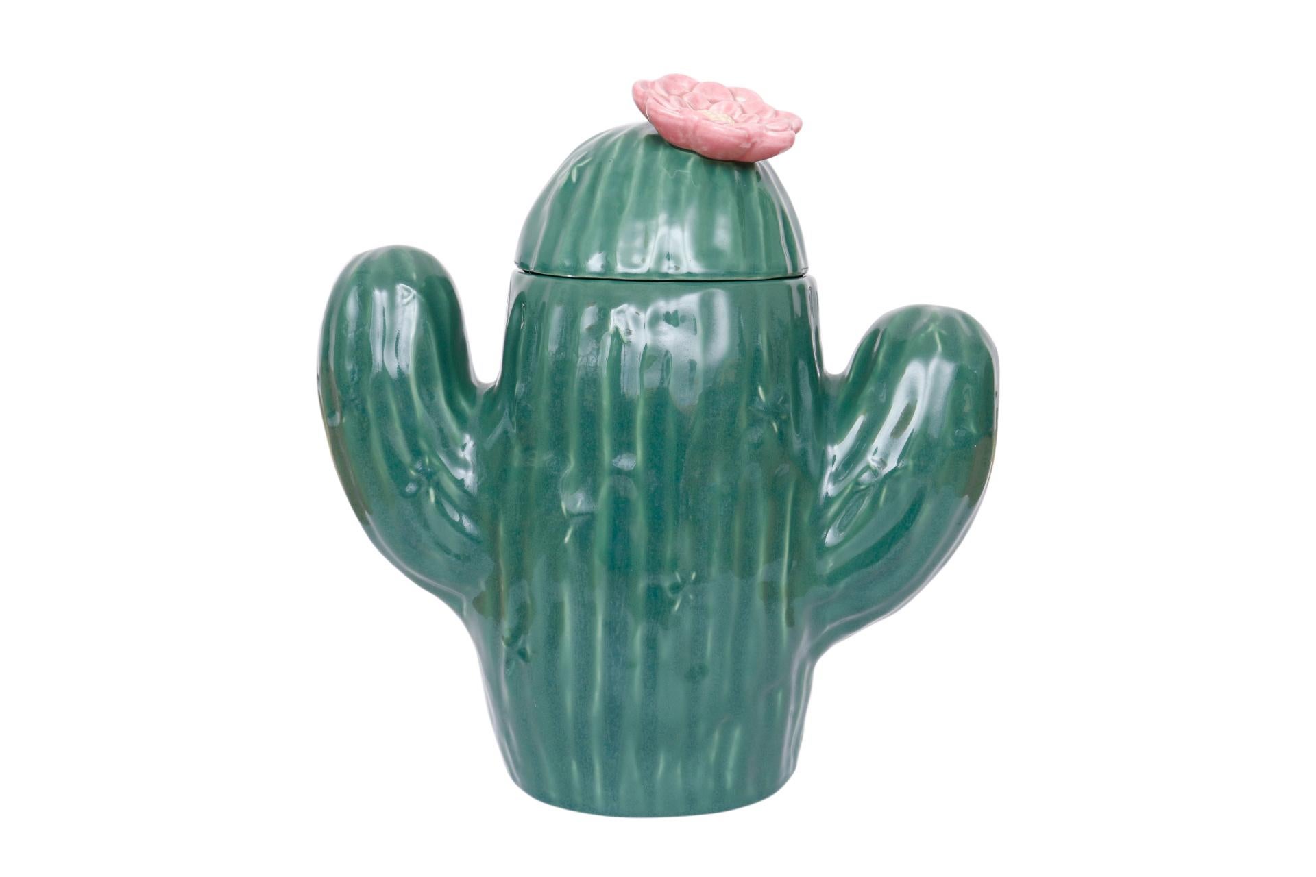 A saguaro cactus shaped cookie jar made by Treasure Craft. Made of ceramic, the jar is decorated with gentle ridges and spines and the lid lifts off with a pink flower for a handle. The maker's name can be seen under the lid.