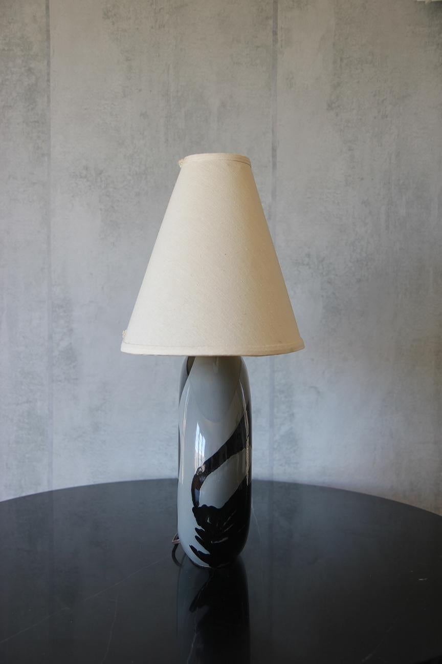 Esta lámpara escultórica de cerámica presenta elementos decorativos inesperados y formas únicas que se integran perfectamente en cualquier espacio, realzando su atractivo estético. Fabricada en cerámica brillante negra y gris, esta lámpara se