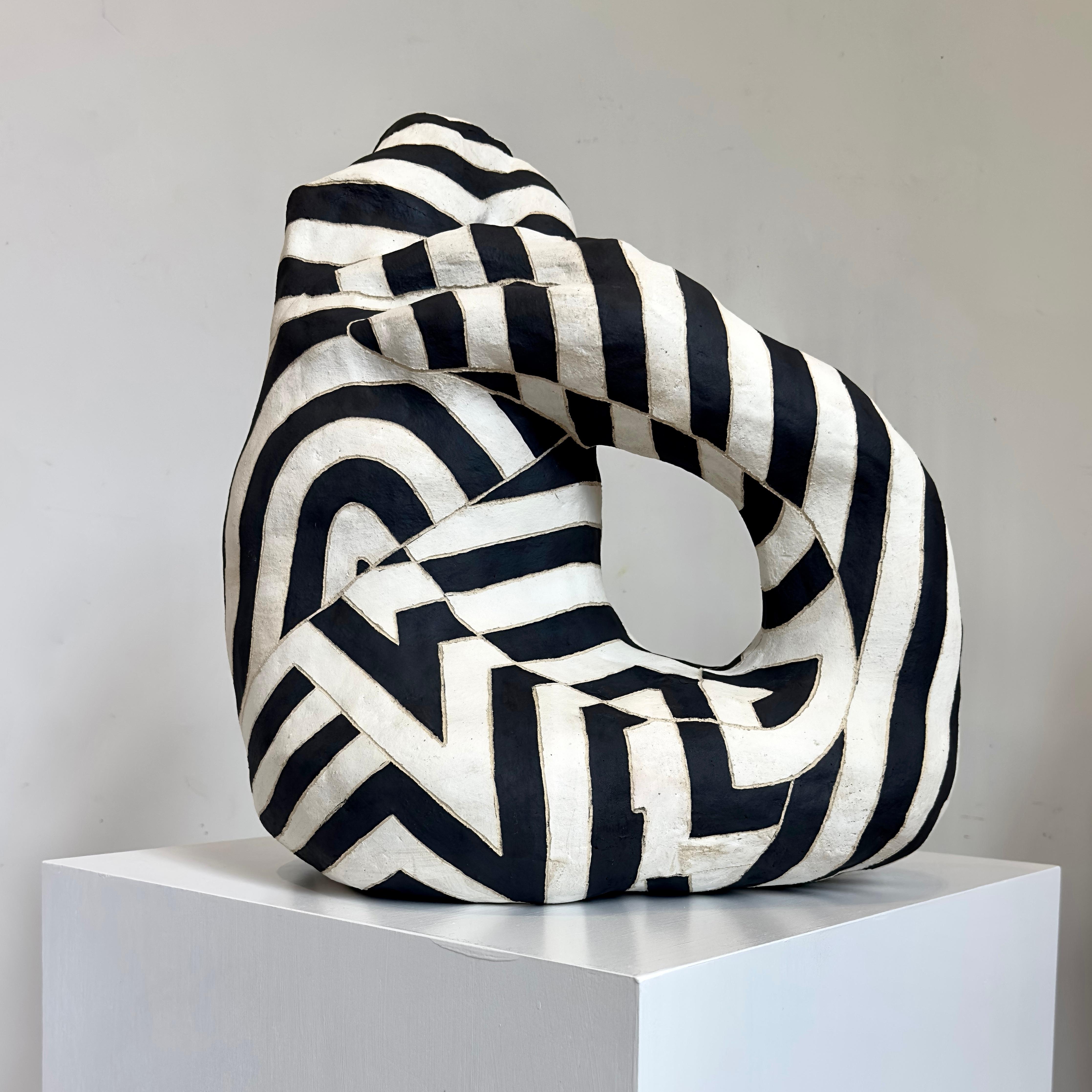 'Cifra' è una scultura astratta in ceramica con motivi superficiali in bianco e nero che si intersecano e si mimetizzano.  La superficie è cerata opaca con bordi incisi sulle strisce.  La scultura ha qualità astratte simili a quelle di un animale e