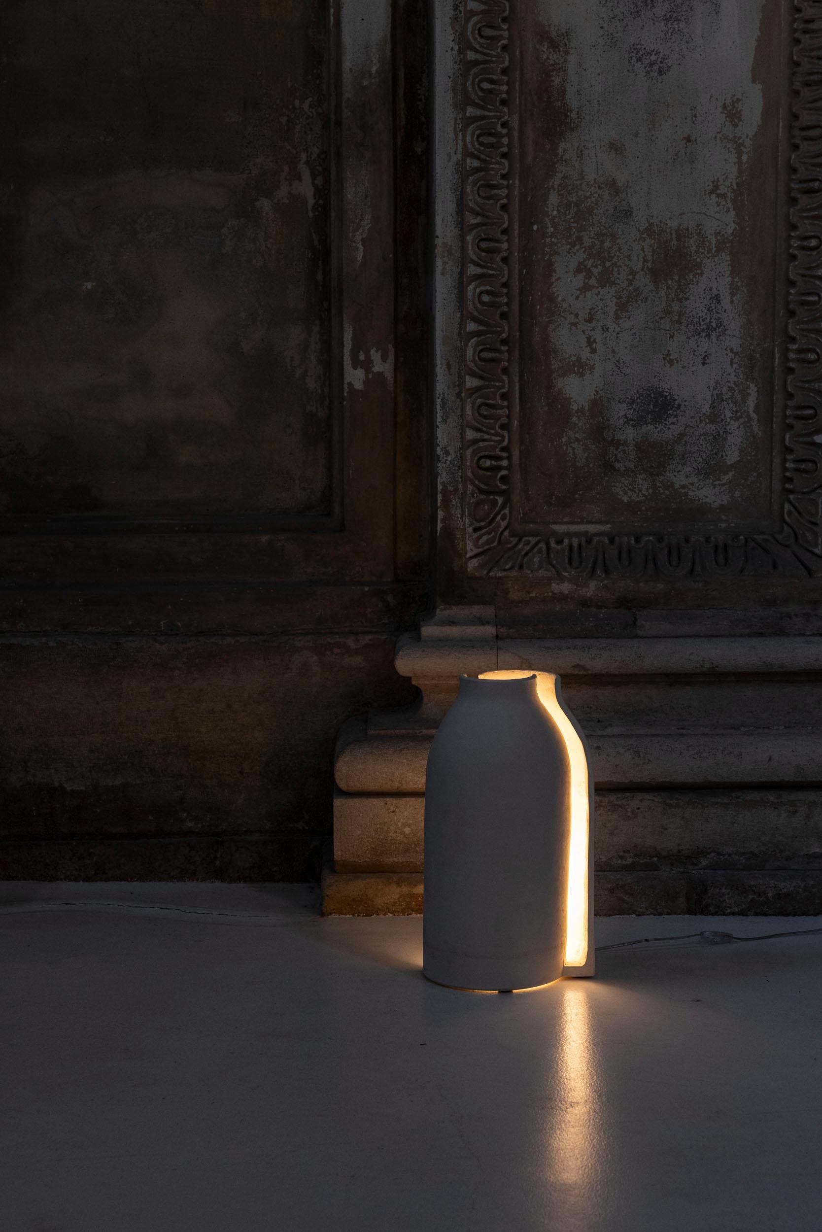 Lampe Mezzaluce conçue et réalisée par Tonino Negri. 
Cette lampe sculpturale en céramique, fabriquée selon la technique de l'enroulement, diffuse une lumière chaude à travers l'ouverture centrale entre ses deux moitiés, créant ainsi une subtile