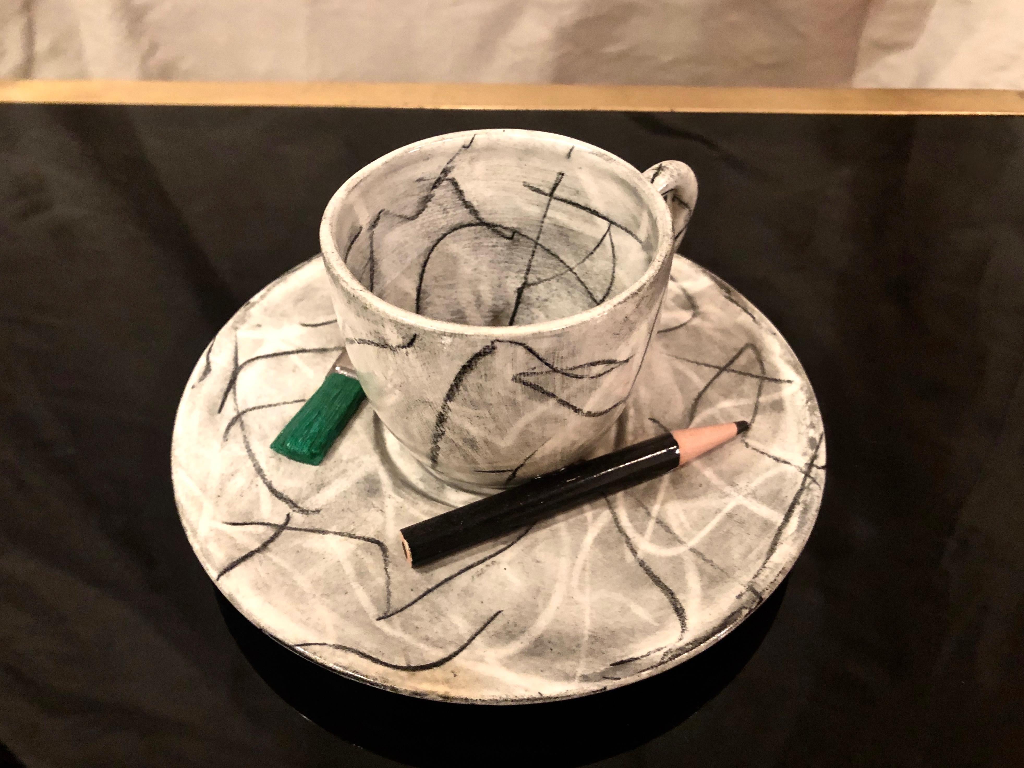 Glazed ceramic sculpture of a tea or espresso cup and plate by American artist David Furman featuring an underglaze, abstract scribble motif and adhered decorative objects of a colored pencil, a typewriter eraser, and a pencil cap eraser. Titled