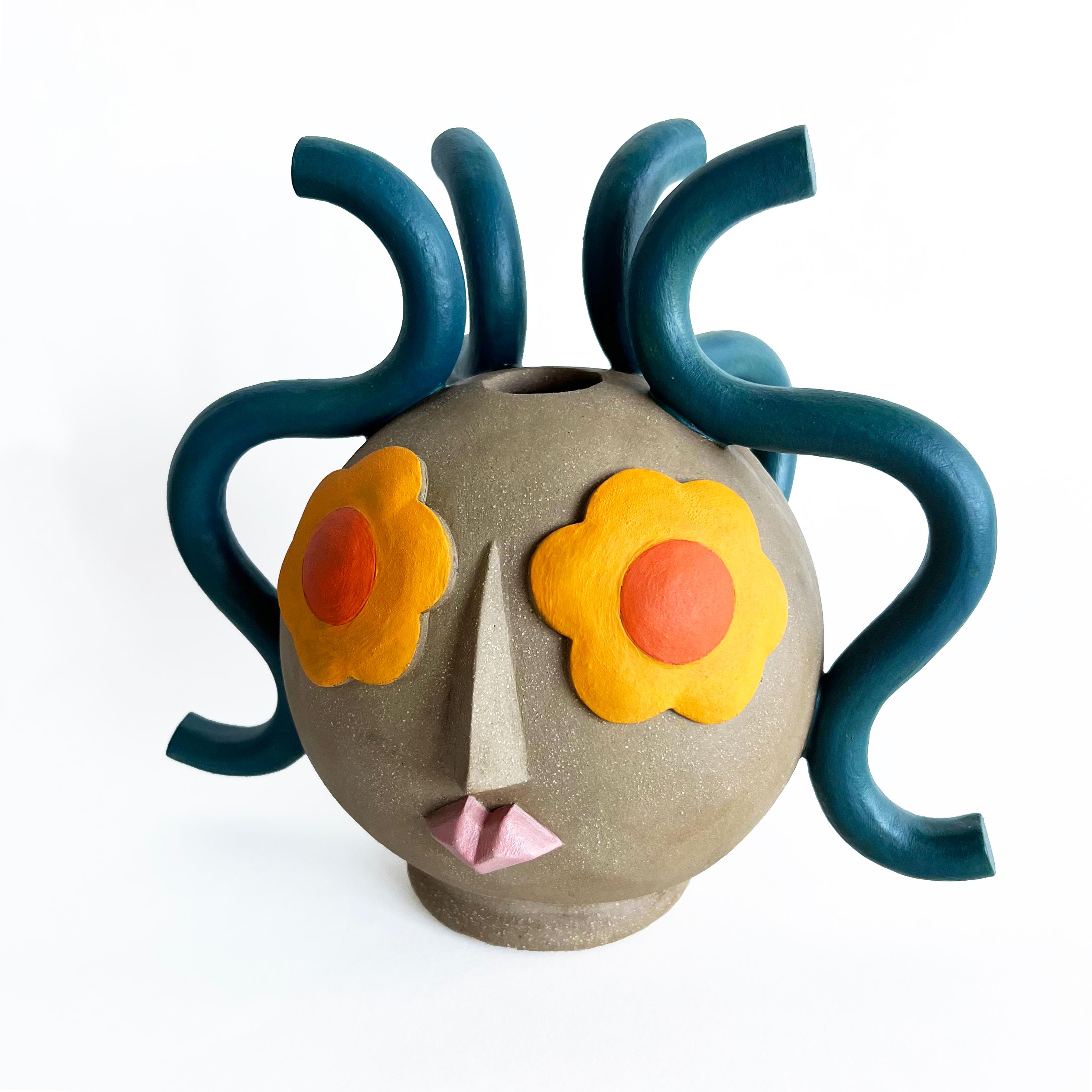 This contemporary figurative vase is handmade by Nashville-based artist, Keavy Murphree. It's hand sculpted in warm brown stoneware with colorful facial features hand-painted with underglaze accents. Rich peacock blue coils of clay create lively