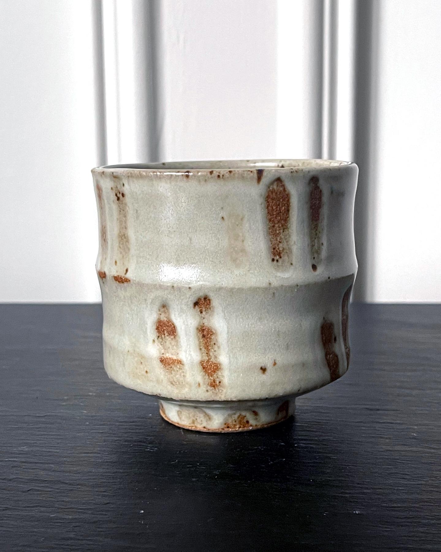 A stoneware tea bowl by American ceramist Warren Mackenzie (1924-2018). Potted in a column shape with a prominent encircling ridged node in the midsection, the upright bowl evokes the silouette of a bamboo trunk. The surface is covered in a milky