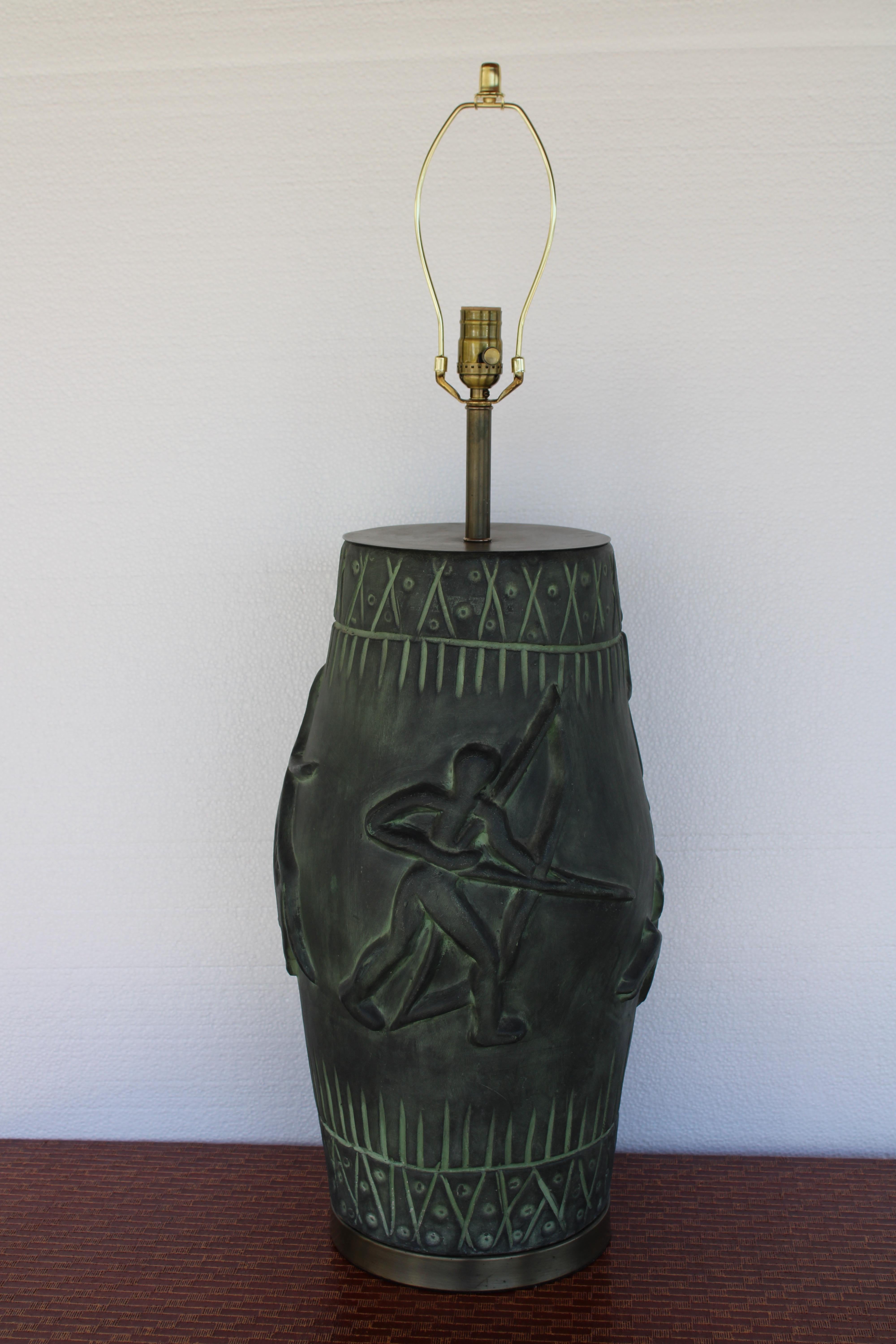 Lampe en céramique et en acier représentant des guerriers chassant avec un arc, des flèches et une lance.  La lampe mesure 27