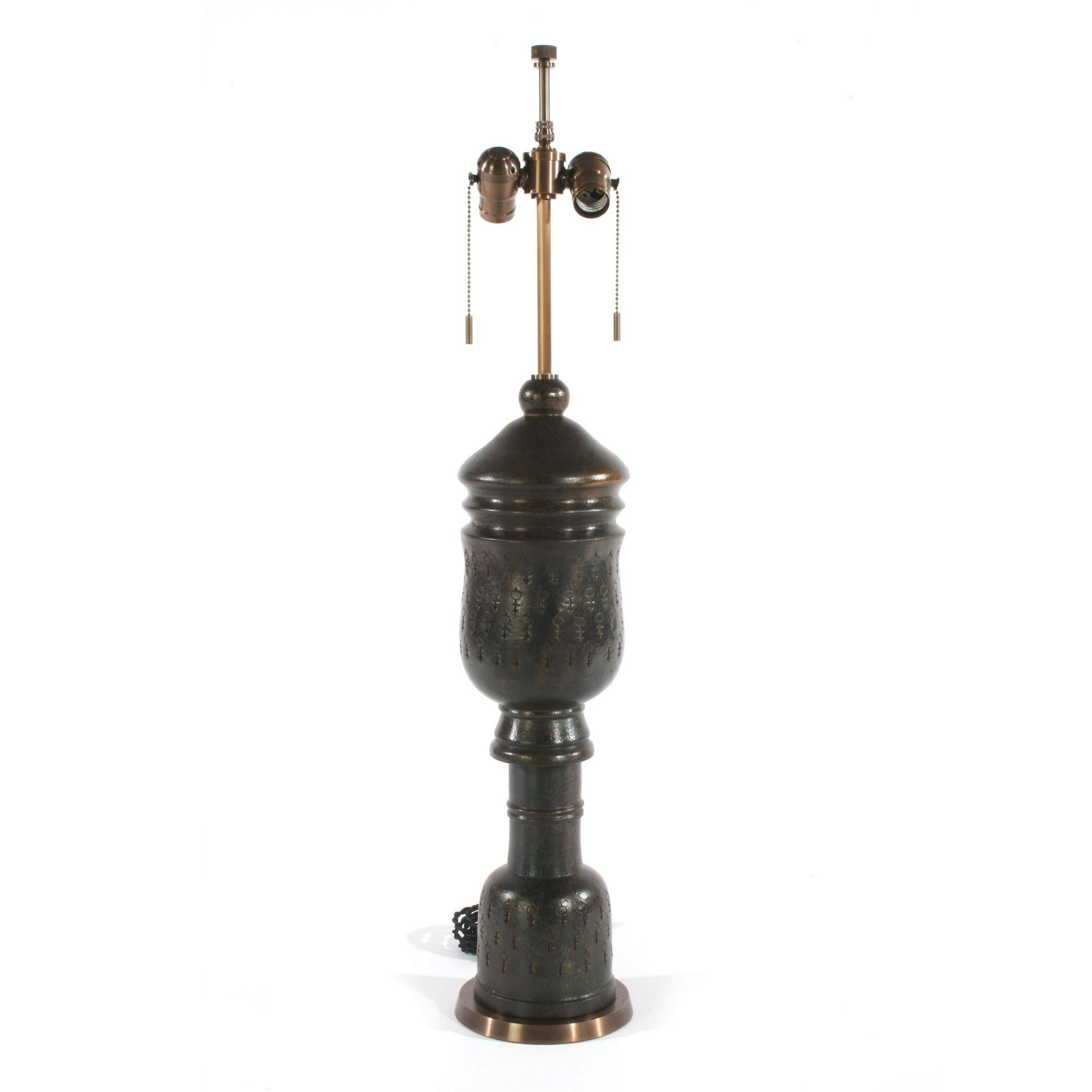 Lampe de table en céramique aux formes élancées, incisée d'un motif représentant le symbole astrologique de Vénus, recouverte d'une riche glaçure foncée sur une base en bronze. Abat-jour non inclus.
