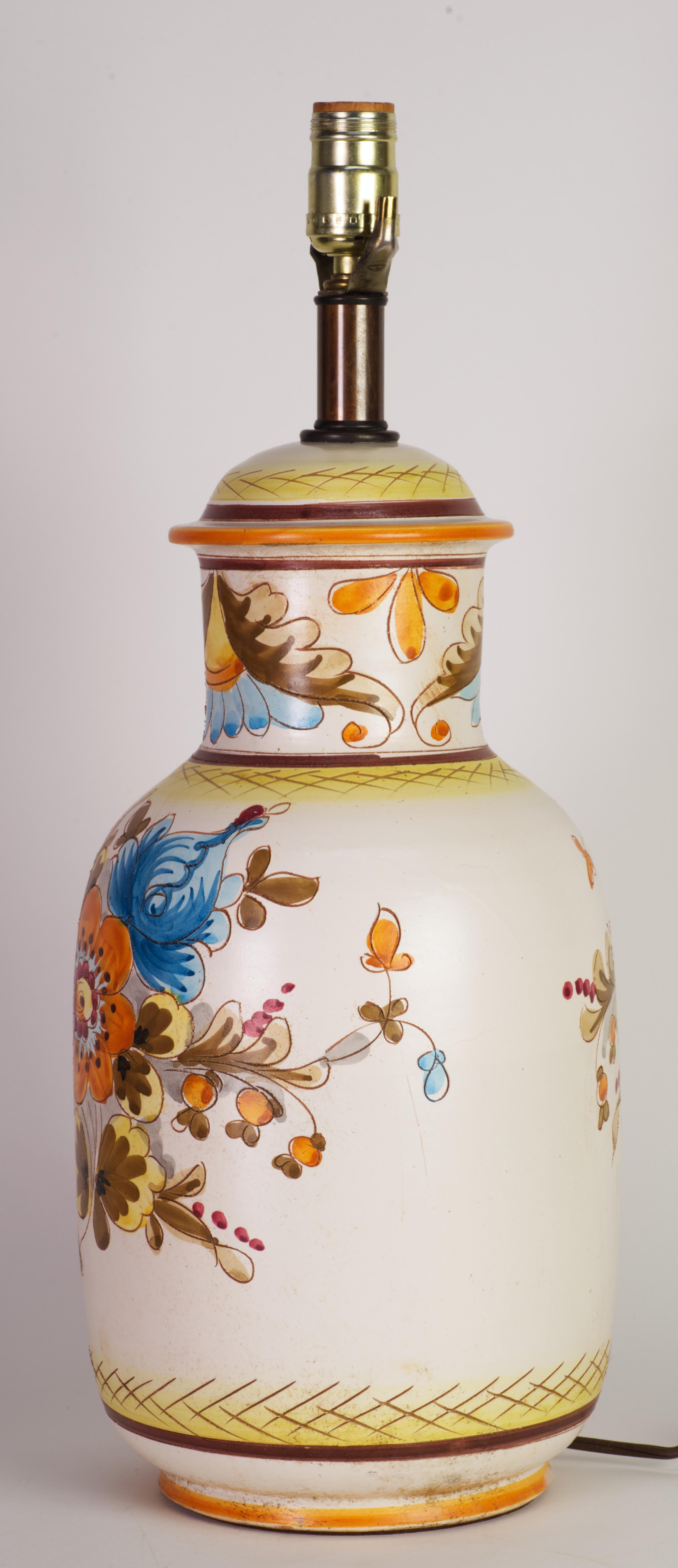 Ceramic table lamp is decorated in European country style with traditional blue and orange floral motifs on semi-matte off-white background. The motif on the back is slightly smaller than motif on the front of the lamp. The neck is adorned with