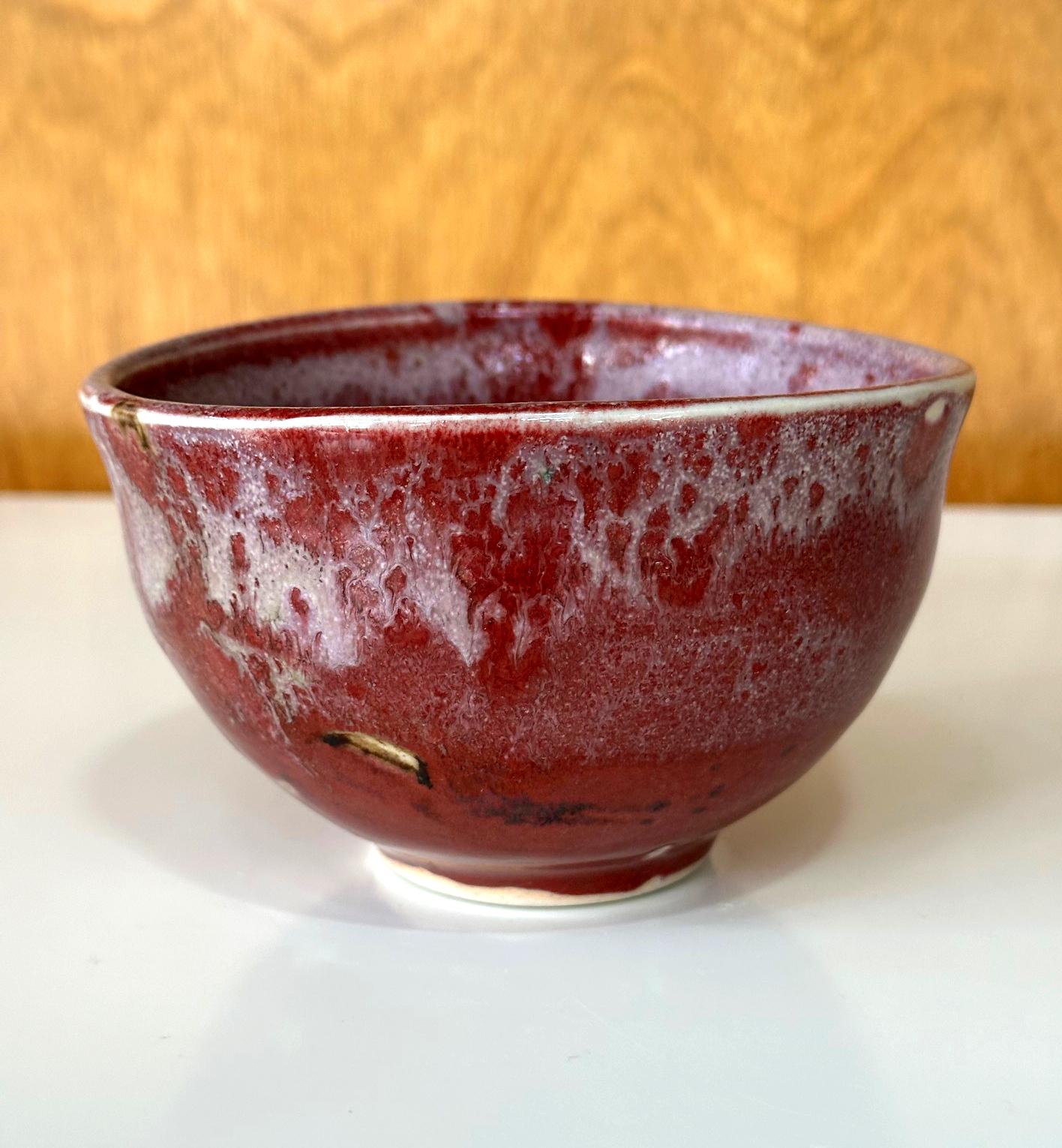 Tazón de té (chawan) de cerámica vidriada, obra de la artista japonesa-estadounidense Toshiko Takaezu (1922-2011). La forma, hecha a mano, muestra una ligera irregularidad y está cubierta de un brillante vidriado de un llamativo rojo fuego con