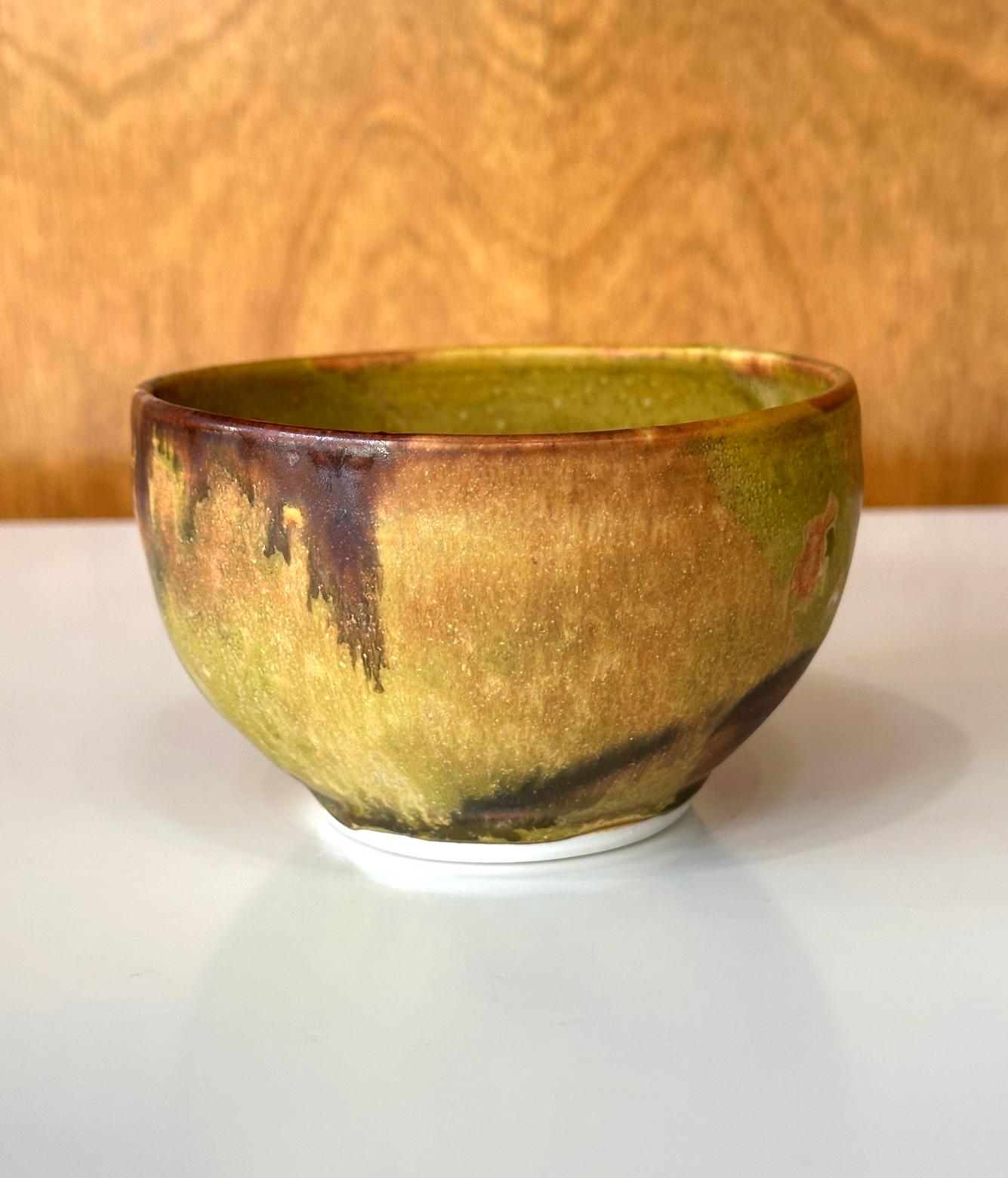 A glazed ceramic tea bowl (chawan) by Japanese American artist Toshiko Takaezu (American, 1922 - 2011). The hand-built bowl is covered with a striking matte glaze in mustard yellow with inclusion of mottled matrix of burnt orange and iron brown and