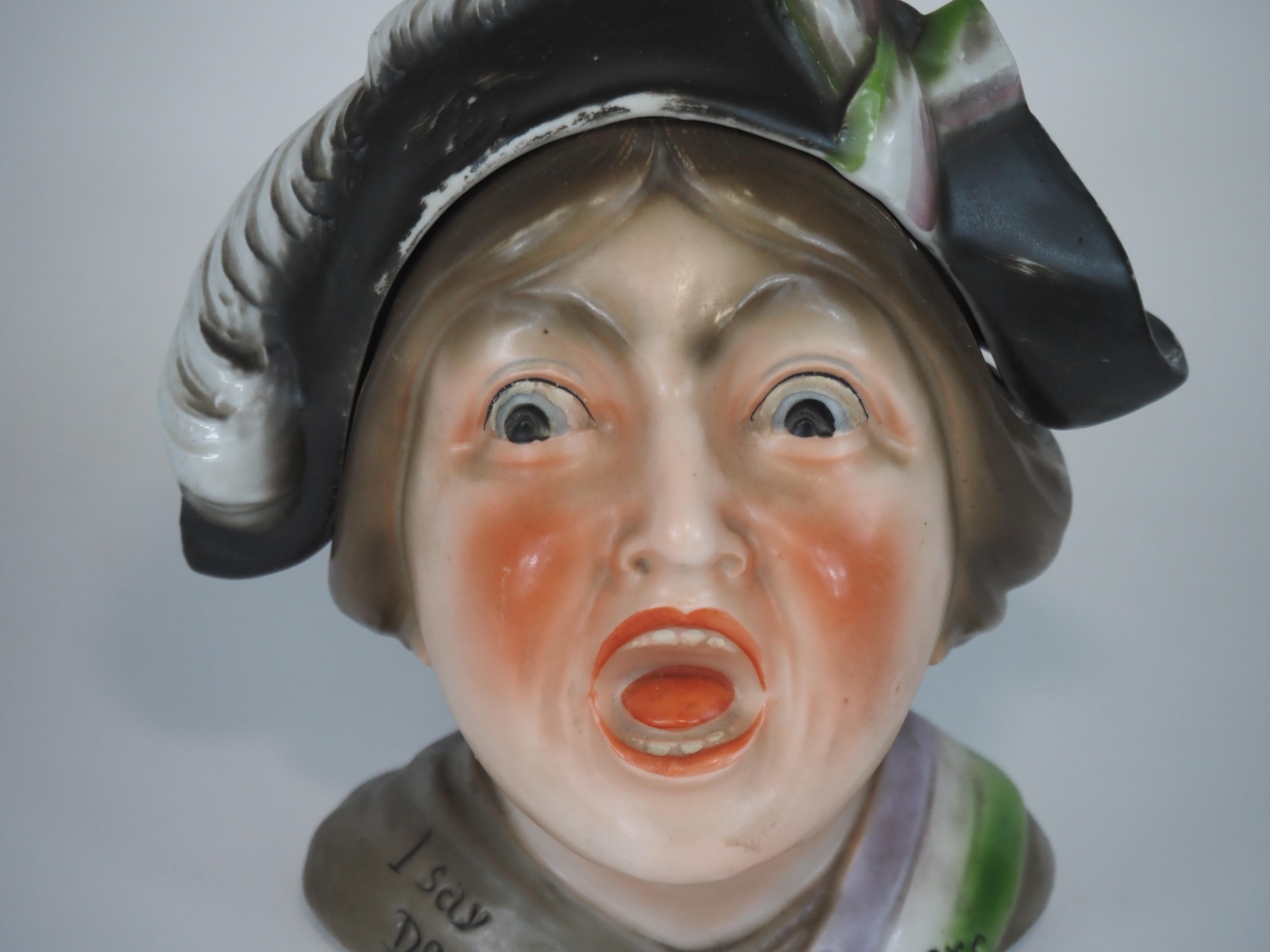 Pot à tabac en céramique en forme de suffragette criant avec un chapeau amovible formant le couvercle.
La femme a de grands yeux et une bouche ouverte. Elle porte les couleurs violette, verte et blanche de la Women's Social and Political Union