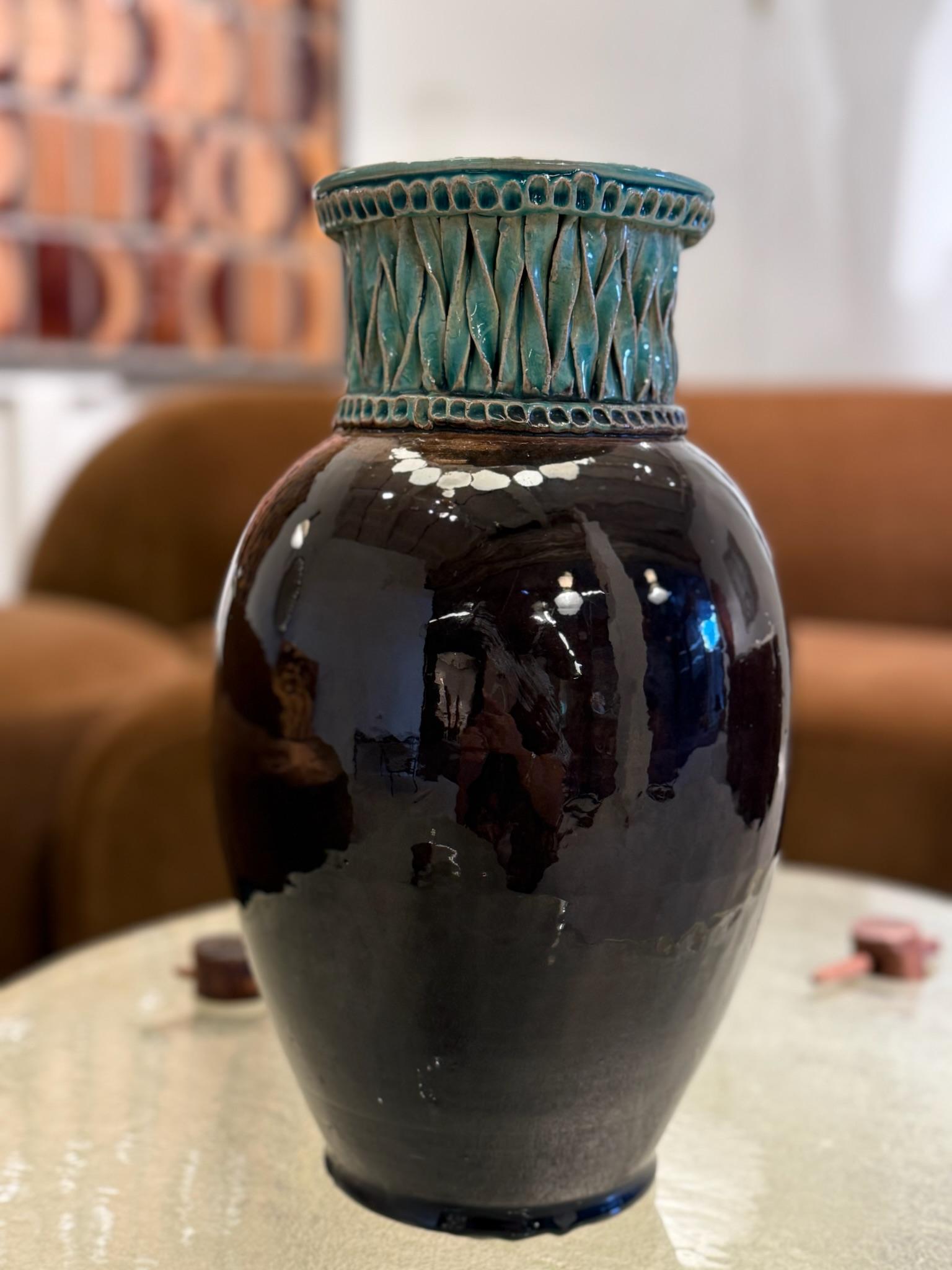 A striking signed ceramic vase featuring a deep, glossy black body contrasted by a textured turquoise neck adorned with geometric relief motifs. This sophisticated interplay of color and texture exemplifies the distinctive artistry of the Accolay