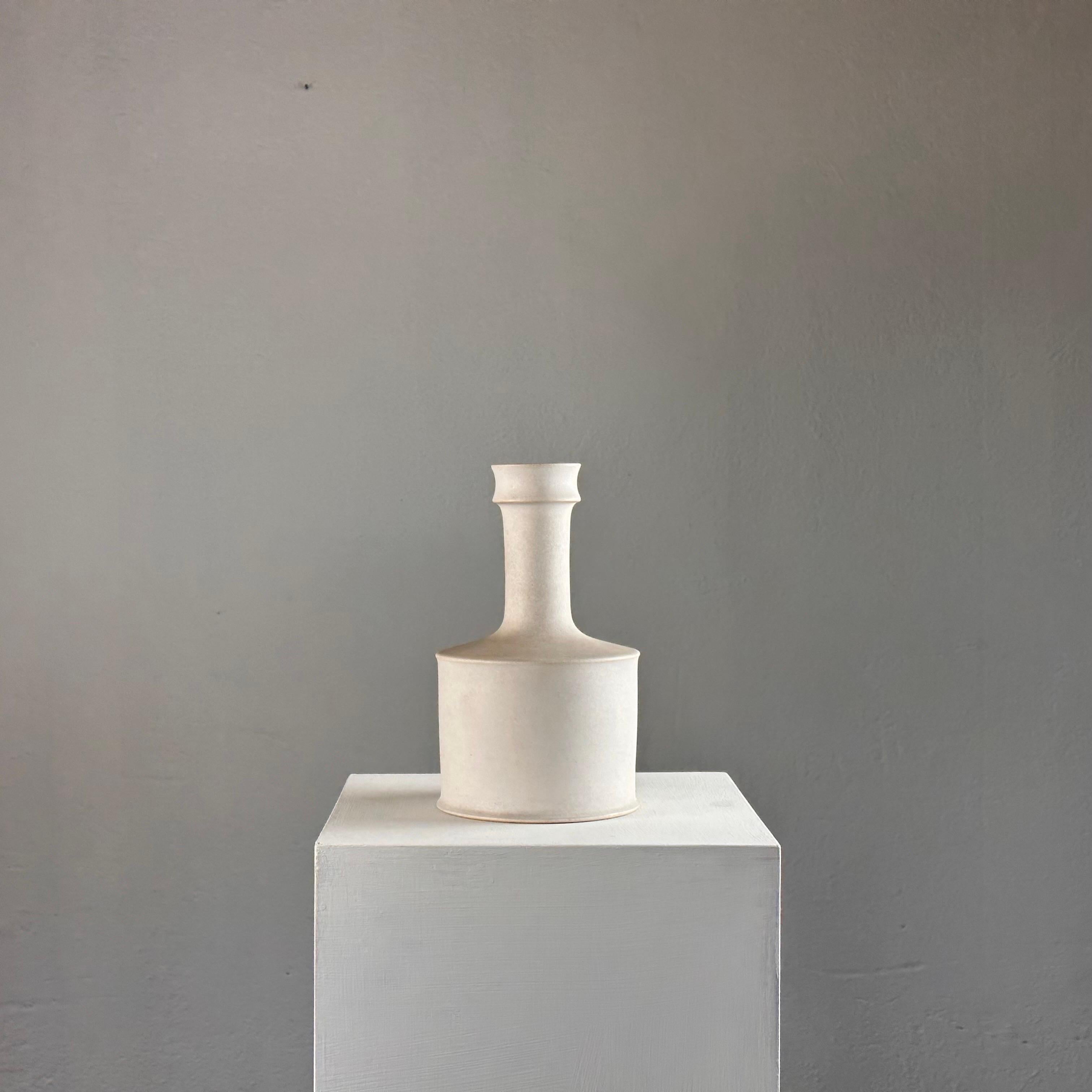 Crafted in the 1960s, this exquisite vase embodies the essence of minimalist sophistication, boasting clean lines and a sleek silhouette.

The vase features a pristine white base adorned with subtly shaded earth-colored profiles, adding depth and