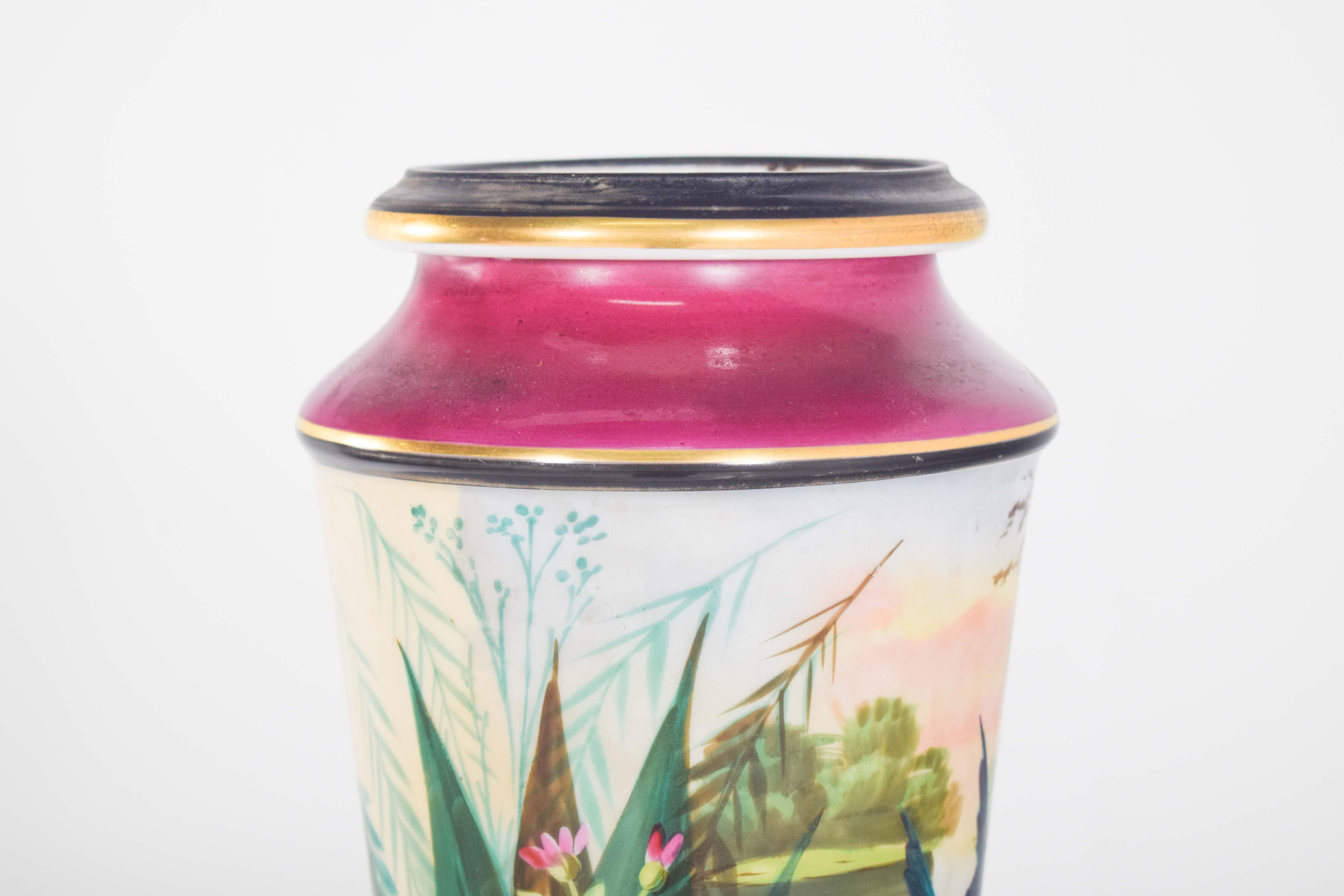 Vaso in ceramica con scena di paesaggio. La decorazione policroma in colori vivaci e oro raffigura un paesaggio fluviale con uccelli, ninfee e piante acquatiche.
Il vaso presenta una vibrante tonalità di rosa-viola ai bordi, sia alla base che alla
