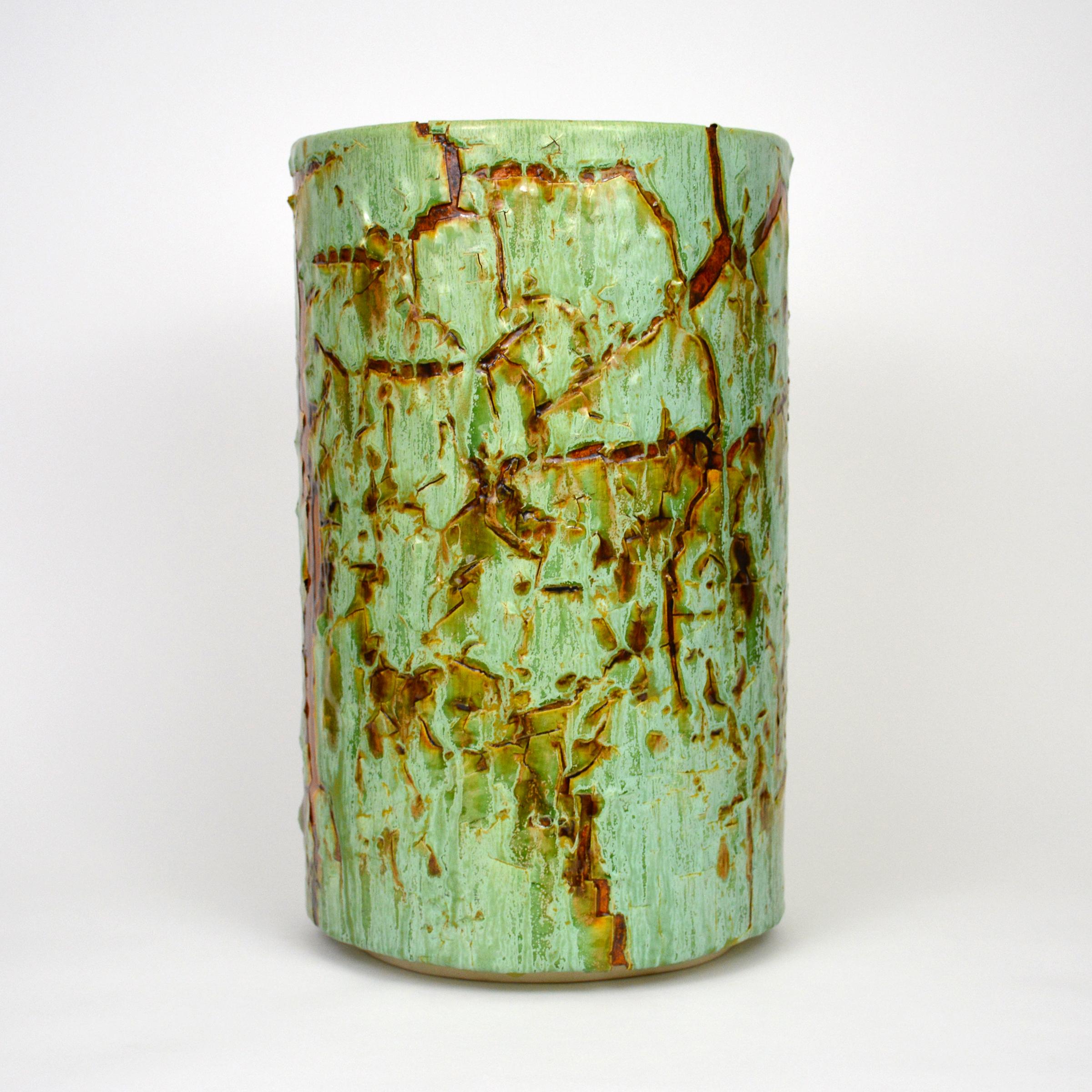 Glazed ceramic cylindrical sculpture by William Edwards
Hand built earthenware vessel, fired multiple times to achieve a textured surface of random abstraction, in hues of green with amber gloss glaze breaking through.

William received his BFA