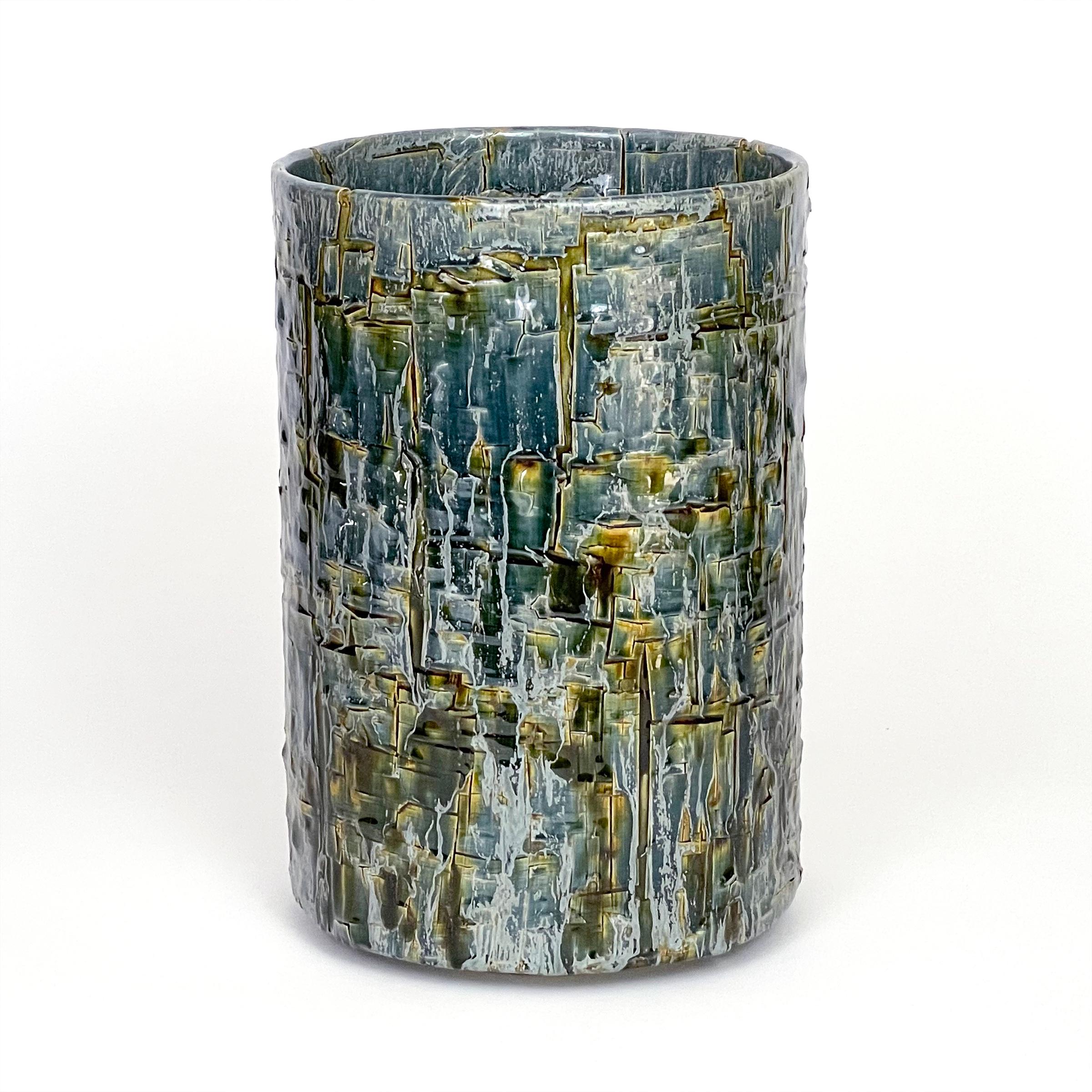 Glazed ceramic cylindrical sculpture by William Edwards
Hand built earthenware decorative vessel, fired multiple times to achieve a textured surface of random abstraction, in hues of blue with amber gloss glaze breaking through.

William received