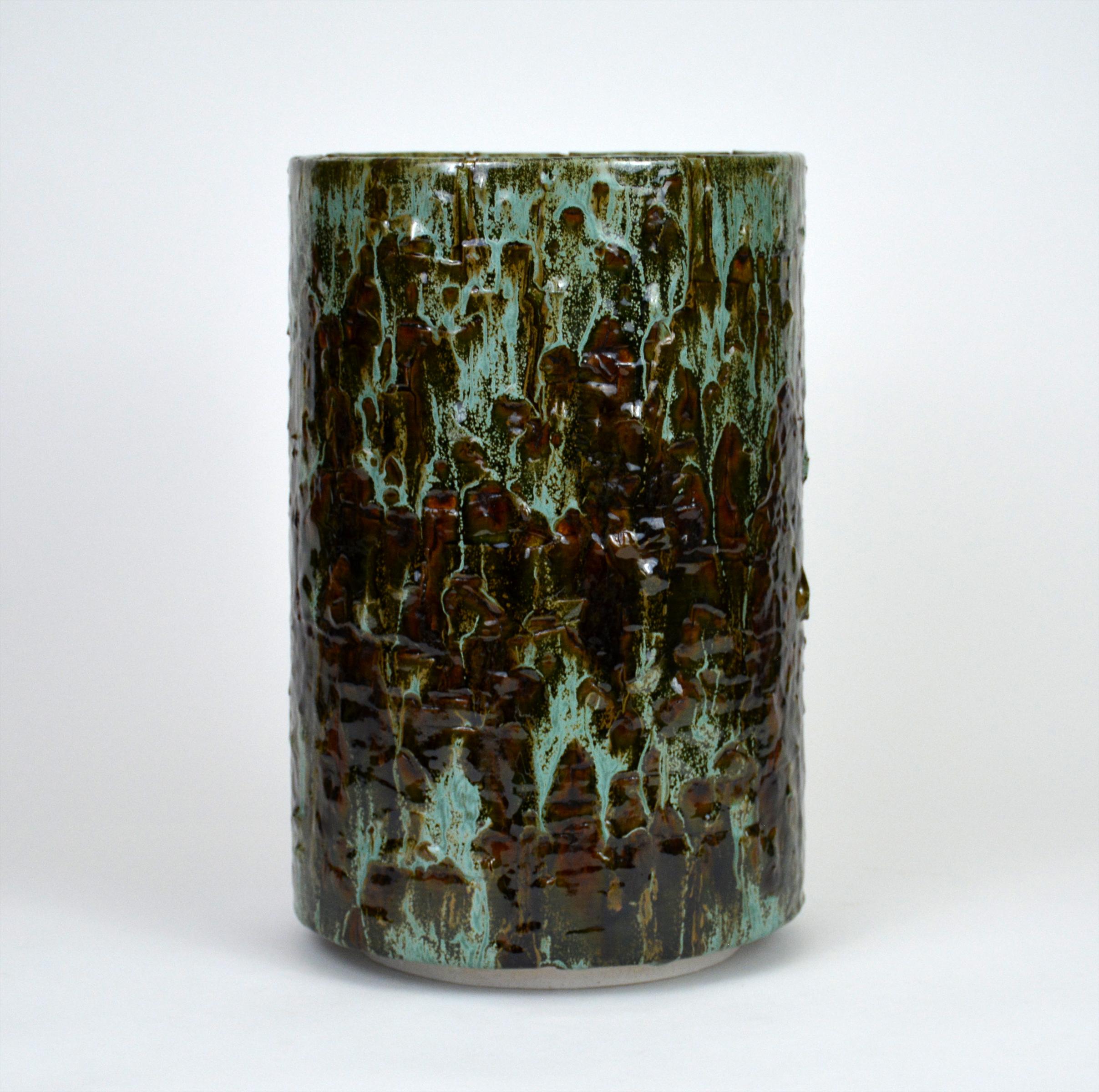 Glazed ceramic cylindrical sculpture by William Edwards
Hand built earthenware decorative vessel, fired multiple times to achieve a textured surface of random abstraction, in hues of green dripping over dark amber gloss glaze.

William received his