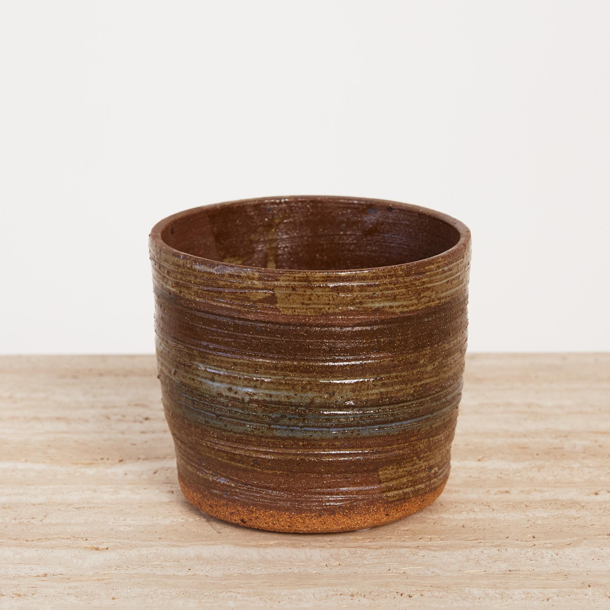 Textured, wide-mouthed ceramic piece perfect as a cup or decorative vessel. The exterior features hand formed striations and organic gradient glaze with rings of golden ochre, burnt umbre, and stone blue. A textured, unglazed, raw ceramic ring lines