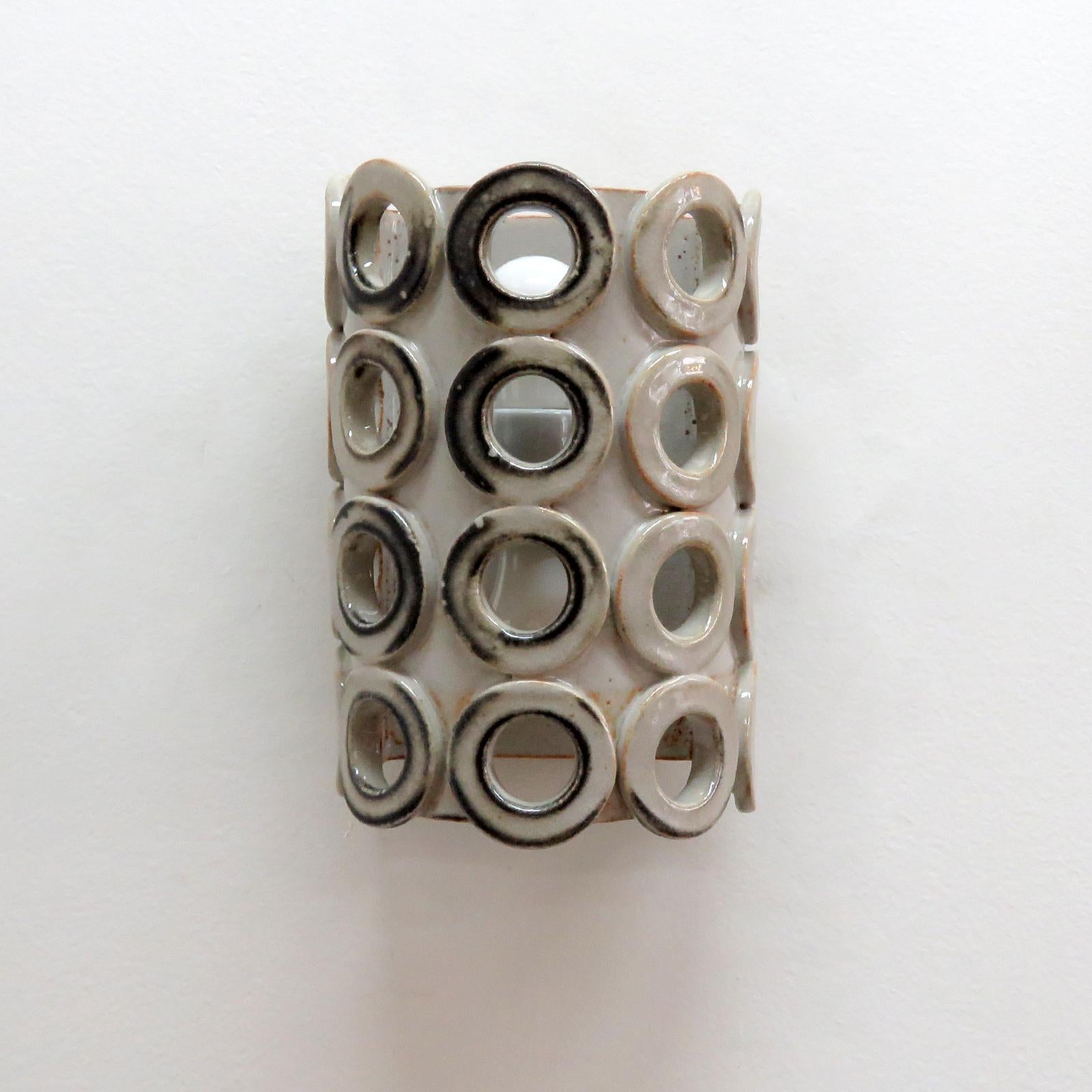 Maravilloso aplique escultórico de cerámica nº 50, diseñado y fabricado a mano por la ceramista Heather Levine, afincada en Los Ángeles. Gres de alta cocción con cuerpo de esmalte de acentos grises y negros con perforaciones decorativas para exponer