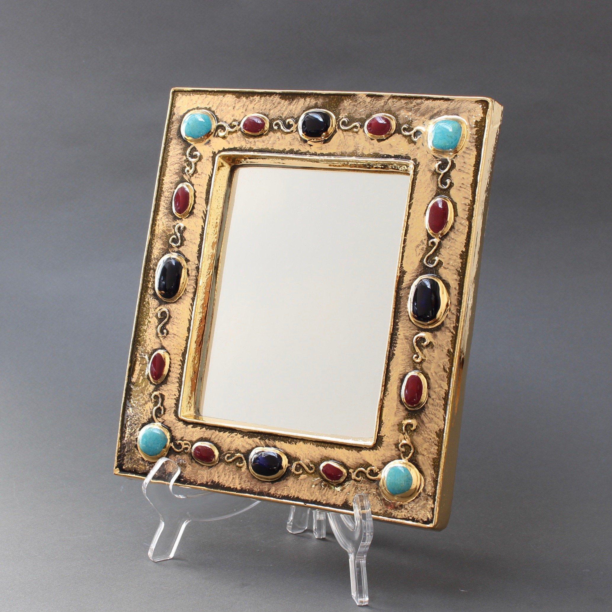 Inspired by Byzantine iconography, a rectangular, gilded glazed ceramic wall mirror by François Lembo (circa 1960s-1970s). With enamelled ceramic cabochons in alternating colours of black, ruby red and turquoise, it is an unusually elegant piece of