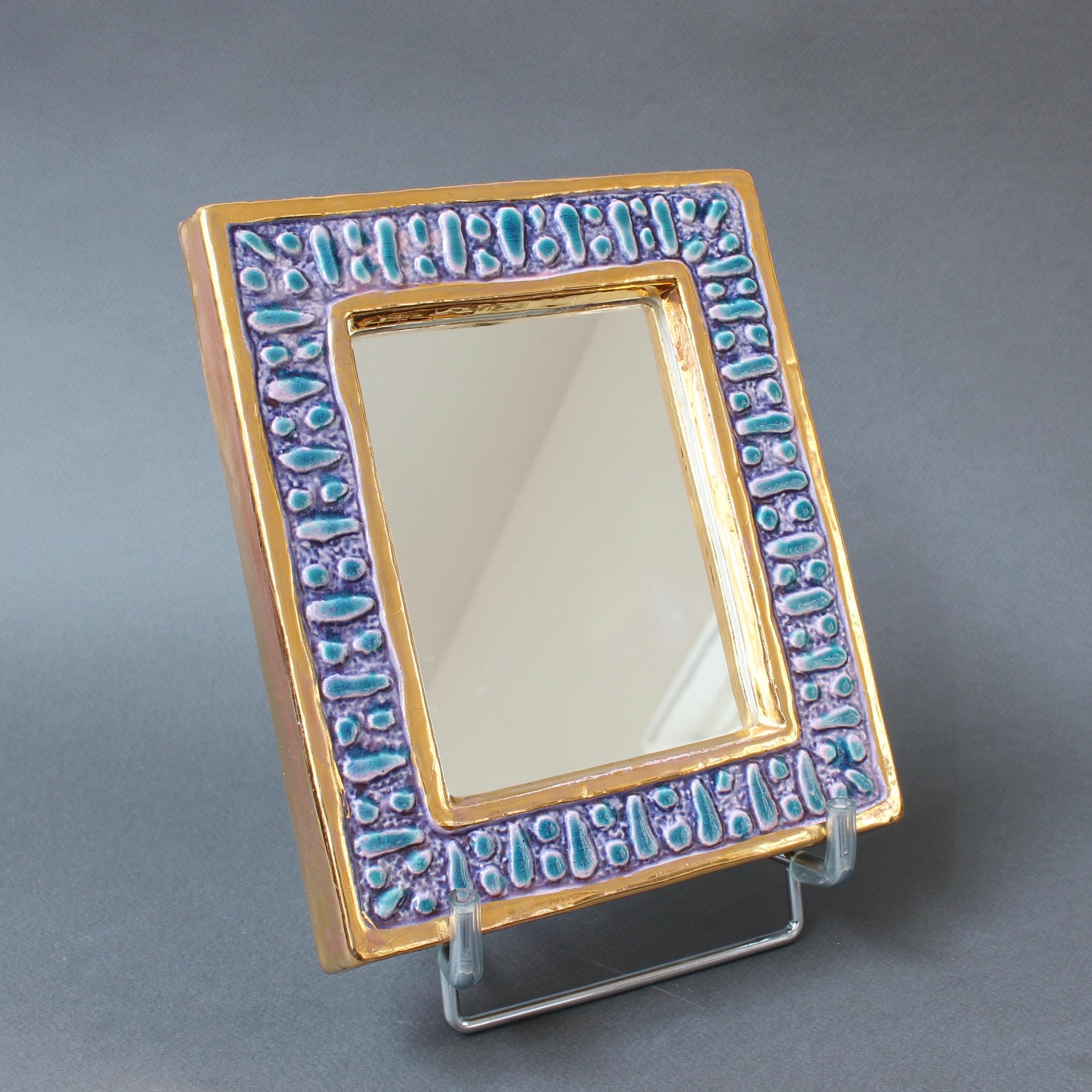 A diminutive ceramic wall mirror with blue enamel glaze and abstract motif (circa 1970s) attributed to François Lembo. A whimsically decorated wall mirror with gold colored inner and outer borders framing a lustrous blue and magenta enamel in a
