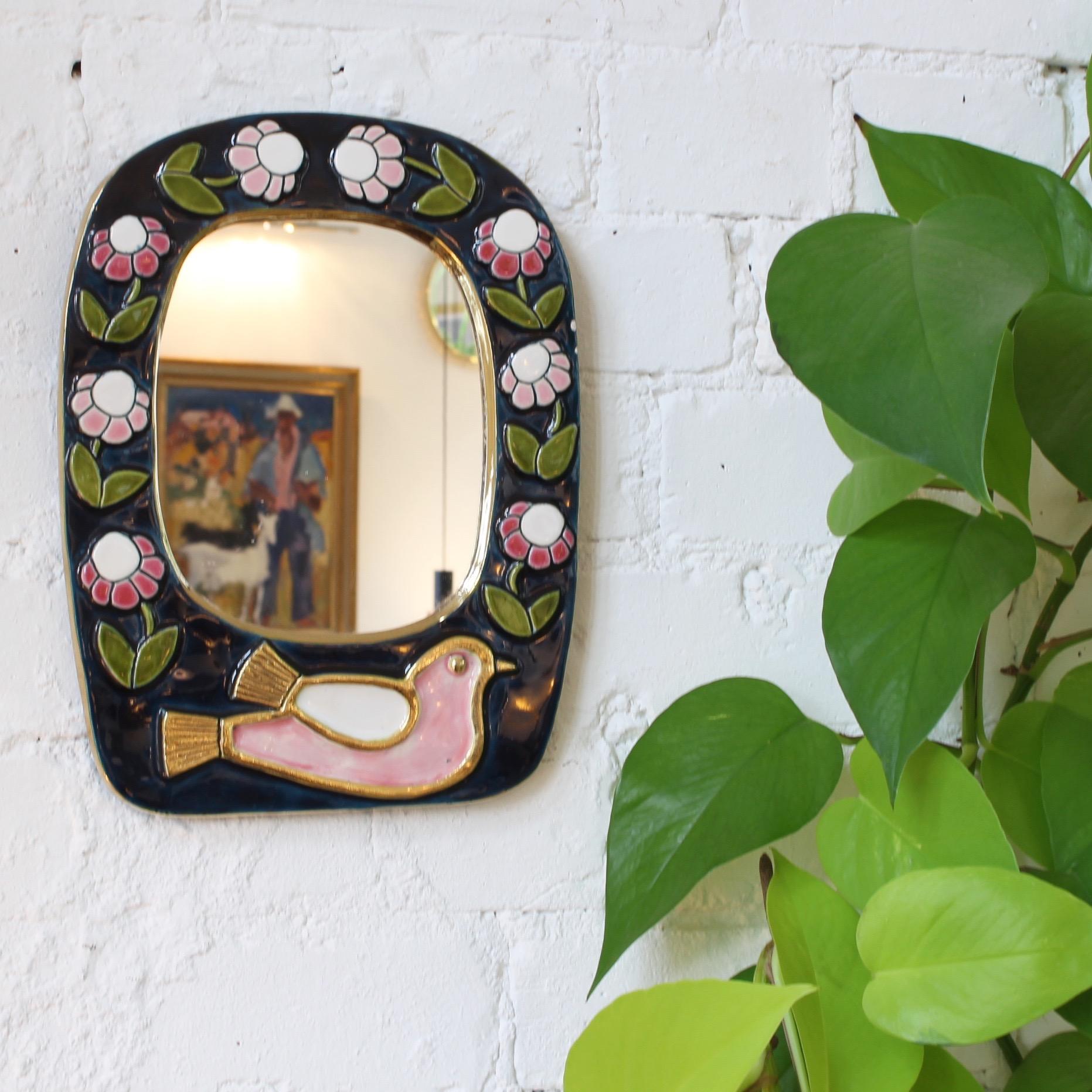 Ceramic wall mirror with enamel glaze, flower motif and stylised bird (circa 1970s) by François Lembo (1930 - 2013). A whimsically decorated wall mirror with gold crackle surround framing a dark blue enamel with pink and red flowers. At the bottom