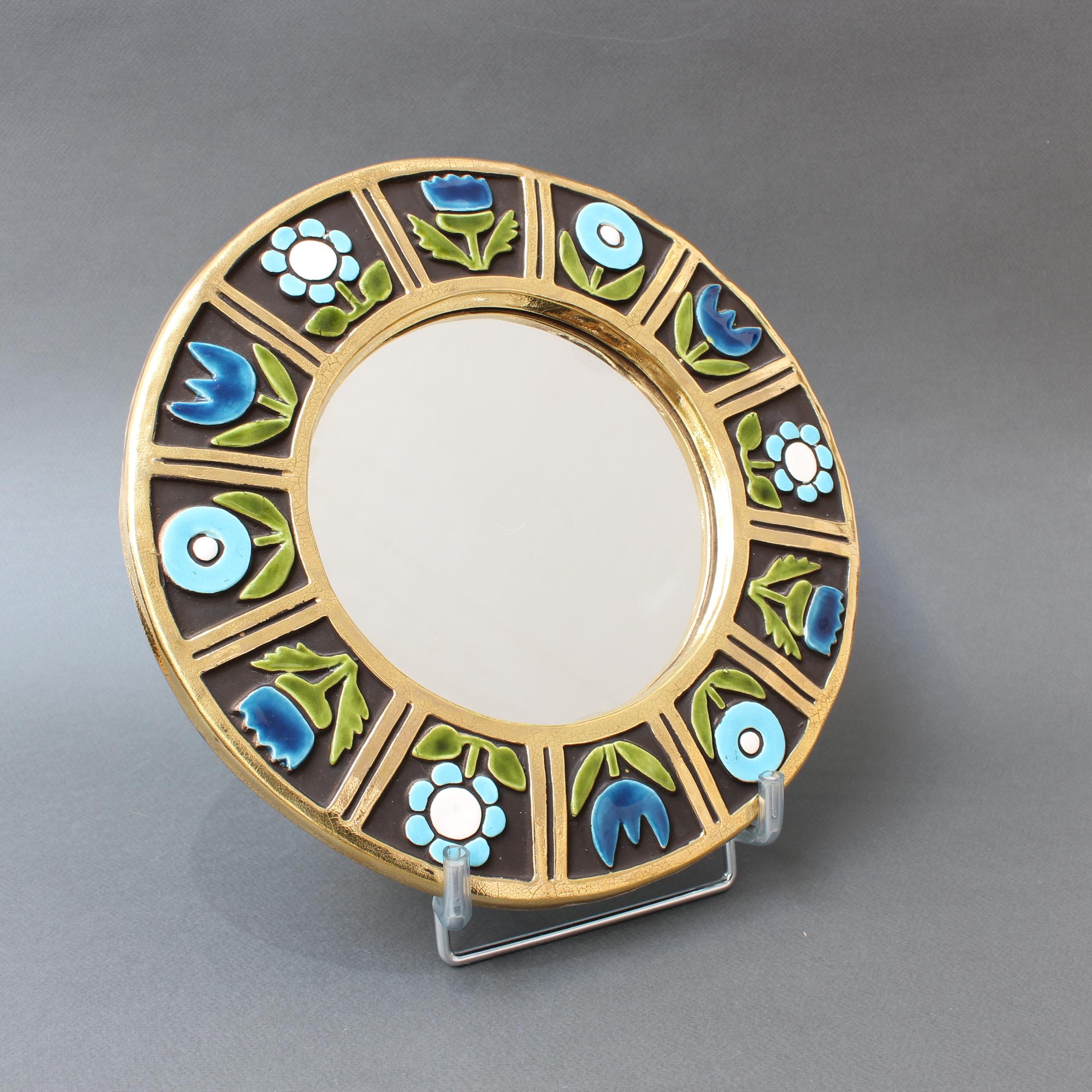 Ceramic wall mirror with flower motif (circa 1960s), by Mithé Espelt. A porthole-shaped decorative wall mirror delights the eye. The inner and outer frames are in a stunning gold craquelure. The enameled flowers are superimposed over a chocolate