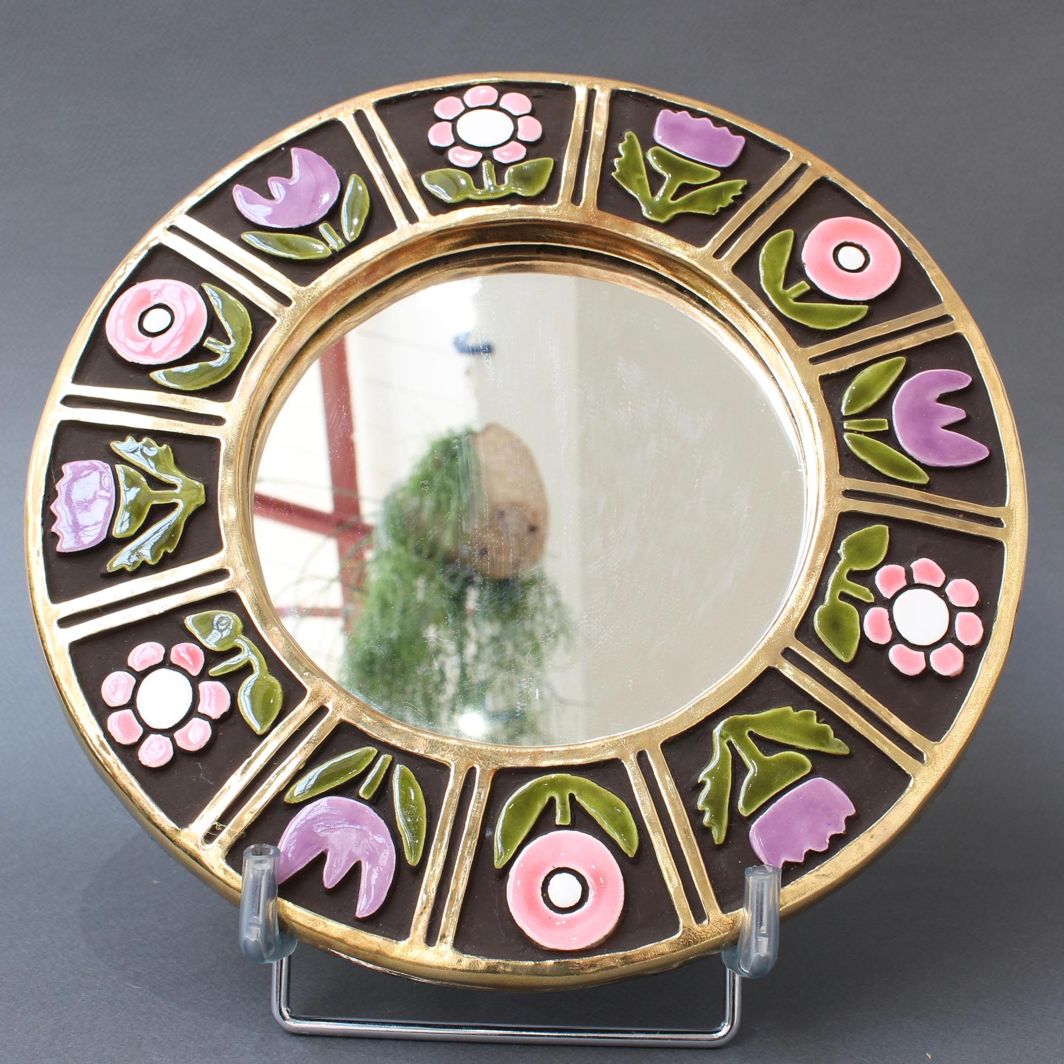 Ceramic wall mirror with flower motif (circa 1960s), by Mithé Espelt. A porthole-shaped decorative wall mirror delights the eye. The inner and outer frames are in a stunning gold craquelure. The enamelled flowers are superimposed over a chocolate
