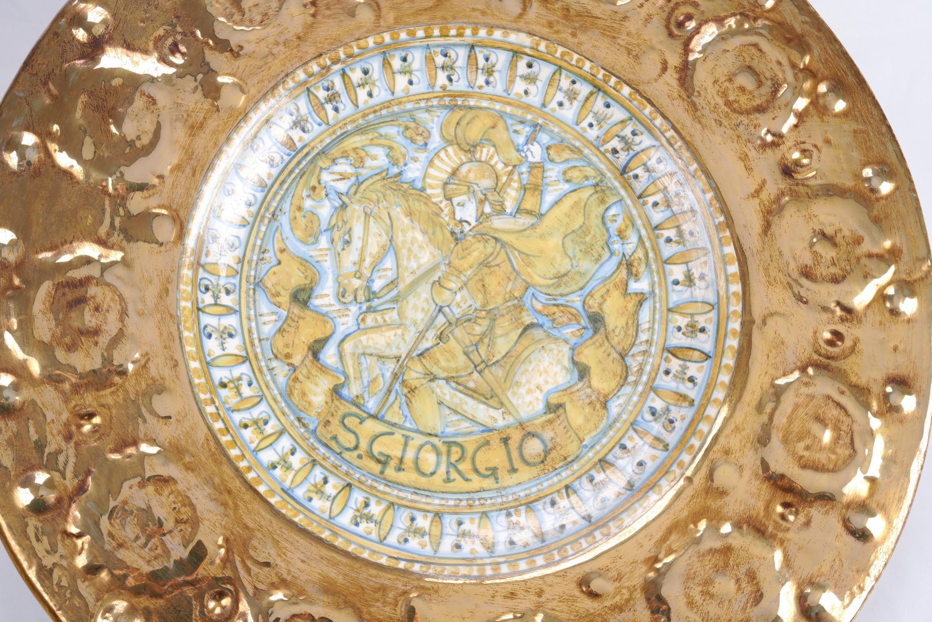 Questo piatto da parete in ceramica, unico nel suo genere e dipinto a mano dal rinomato ceramista italiano Gabriele Mengoni, è un'opera d'arte straordinaria che raffigura il leggendario Saint George. Dipinta in tenui toni seppia e azzurri, la