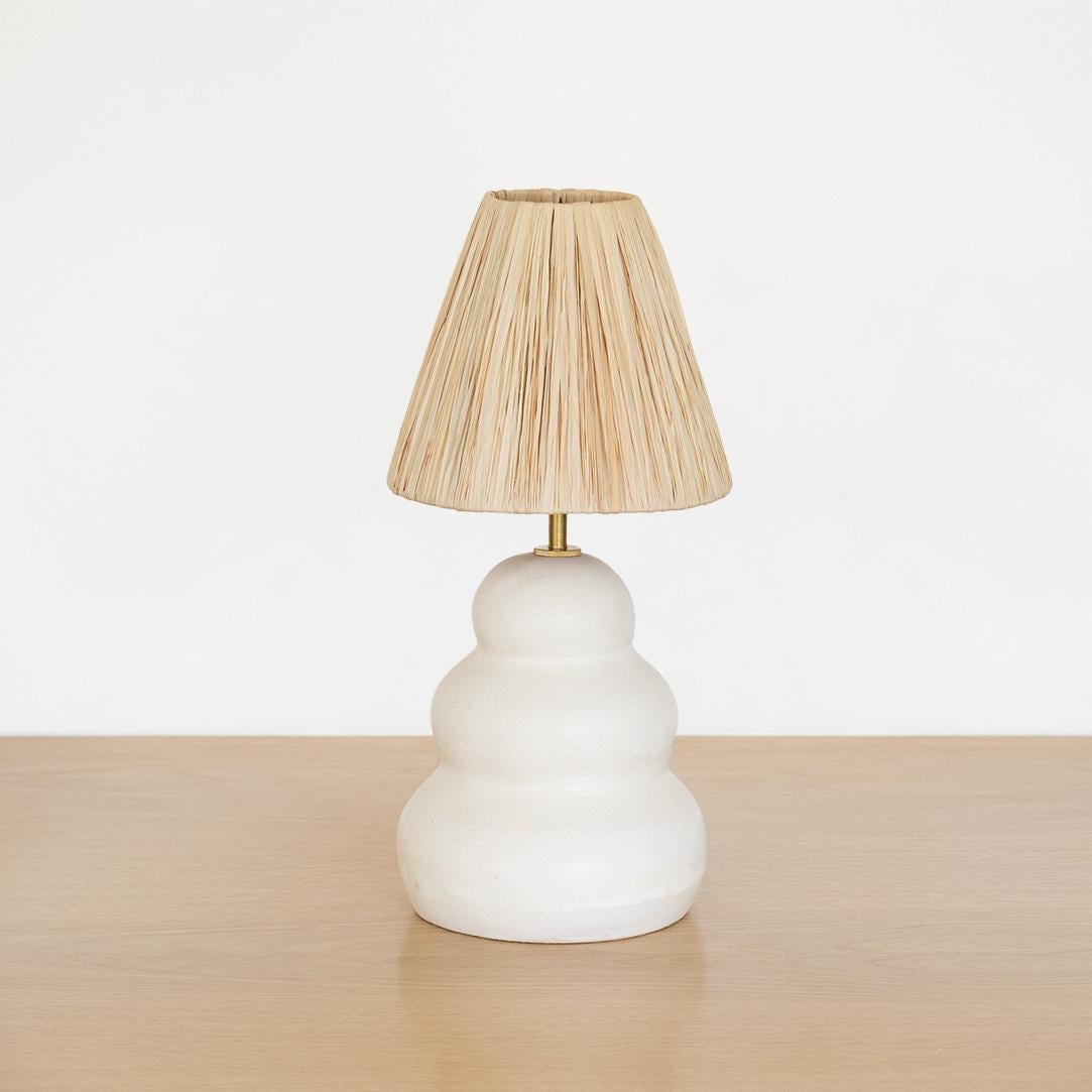 Lampe en céramique de fabrication récente, en forme de colonne ondulée, faite à la main en terre cuite et émail blanc. Nouvel abat-jour en raphia naturel, col de tige en laiton, et nouveau cordon en tissu blanc avec interrupteur. Une forme organique